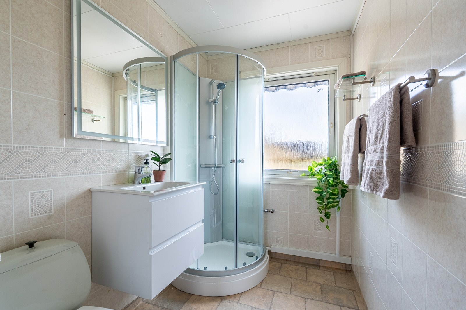 Badet har en standard baderomsinnredning med servant og praktiske skuffer under, klosett og dusjkabinett. Rommet fremstår lyst og trivelig, med en enkel og funksjonell utforming som dekker de daglige behovene på en god måte. Galleribilde