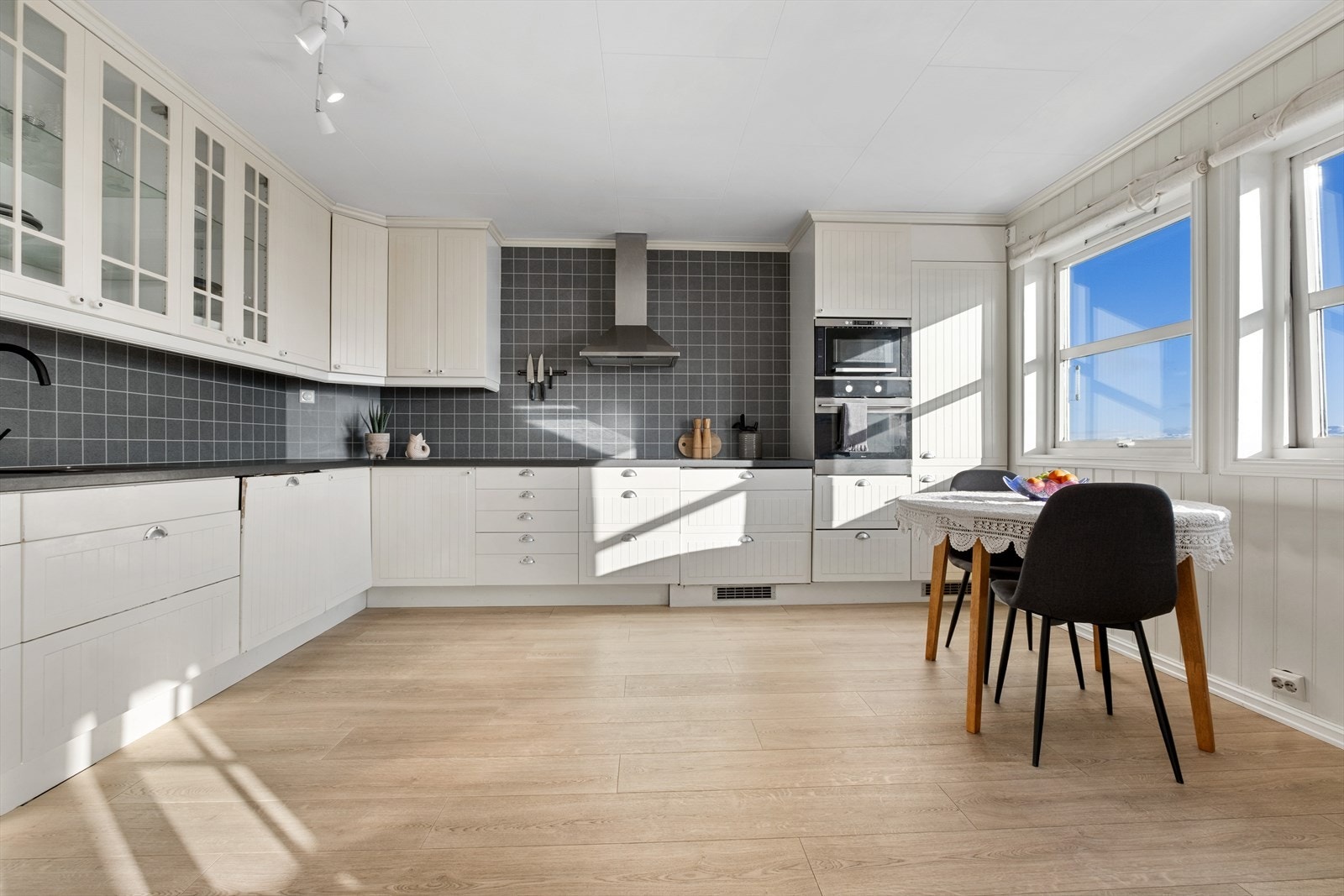 Kjøkkenet er lyst og pent med takhøye overskap, flere vitrineskap og benkeplate i mørk laminat. Galleribilde