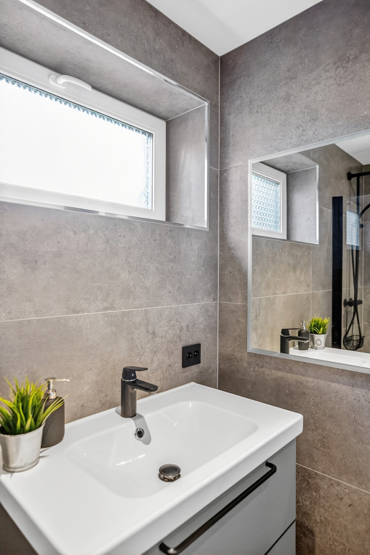 Badet har hvit innfelt vask med sort armatur, stort speil og naturlig lys fra vindu Galleribilde