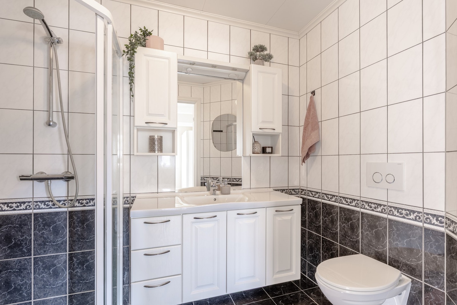 Badet er innredet med vegghengt toalett, dusj med glassvegger, og baderomsmøblement med speil og belysning. Galleribilde