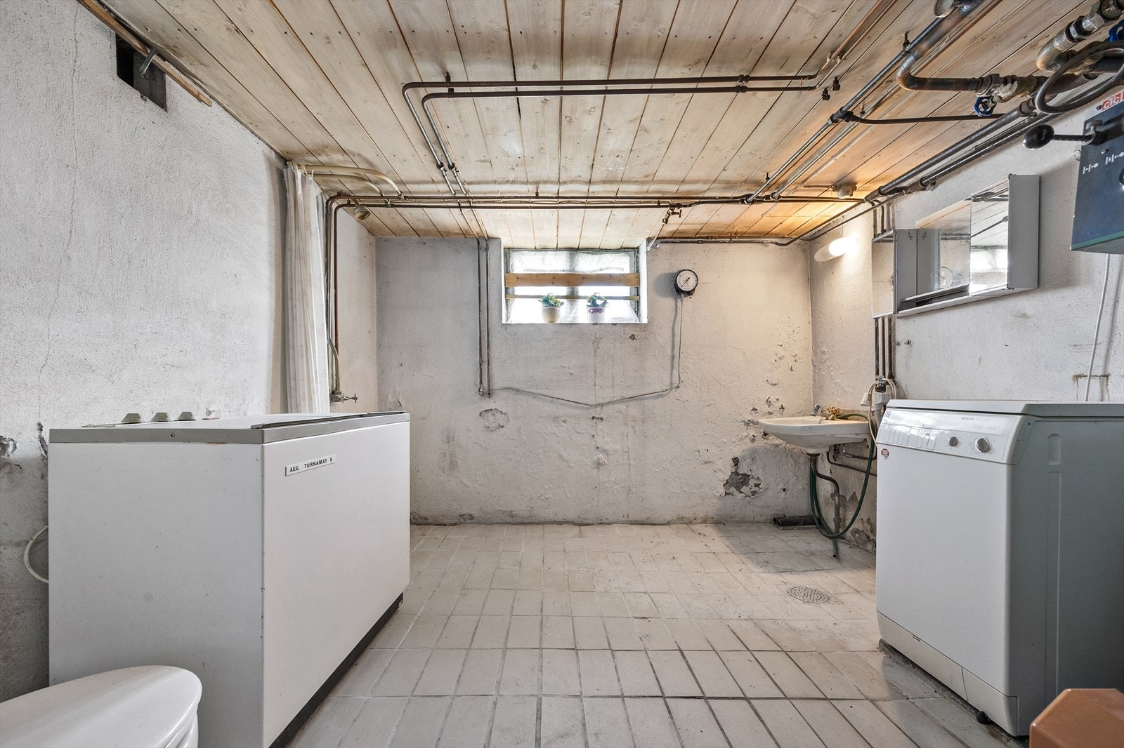 Vaskerommet i kjelleren har betongoverflater, opplegg for vaskemaskin og plassering av fyrkjele. Galleribilde