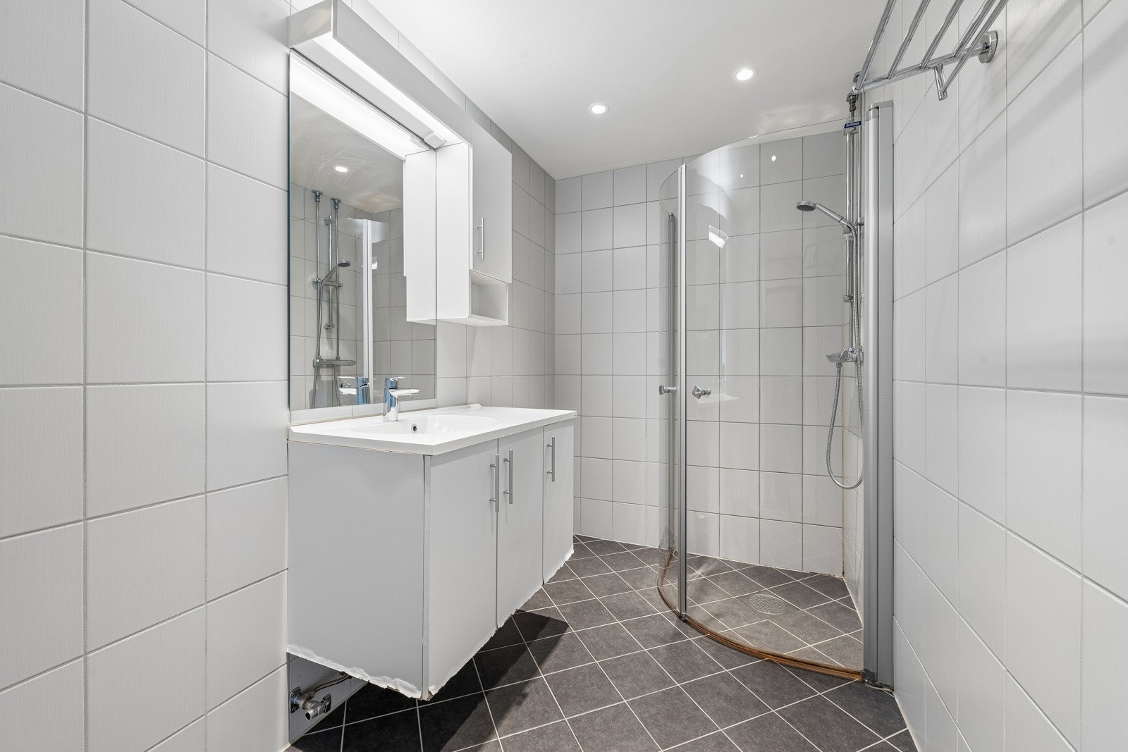 Badet fra 2018 har varmekabler i gulv og downlights i tak og inneholder servant og dusj i hjørne med innadslående dører. Galleribilde