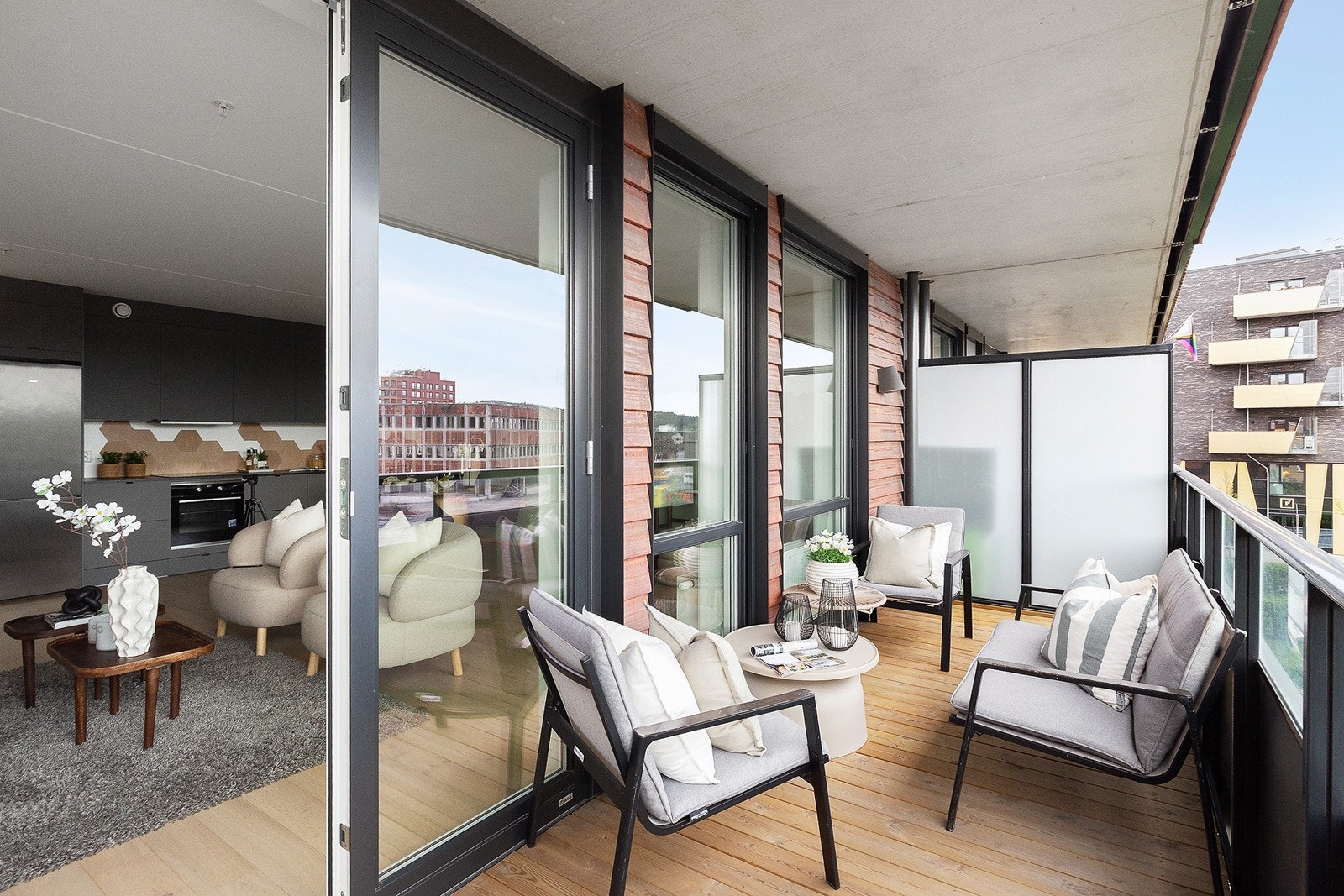 Syd-sydvestvendt balkong på 10m² med tregulv, belysning, strømuttak, rekkverk med glass øverst og adkomst fra stue. Galleribilde