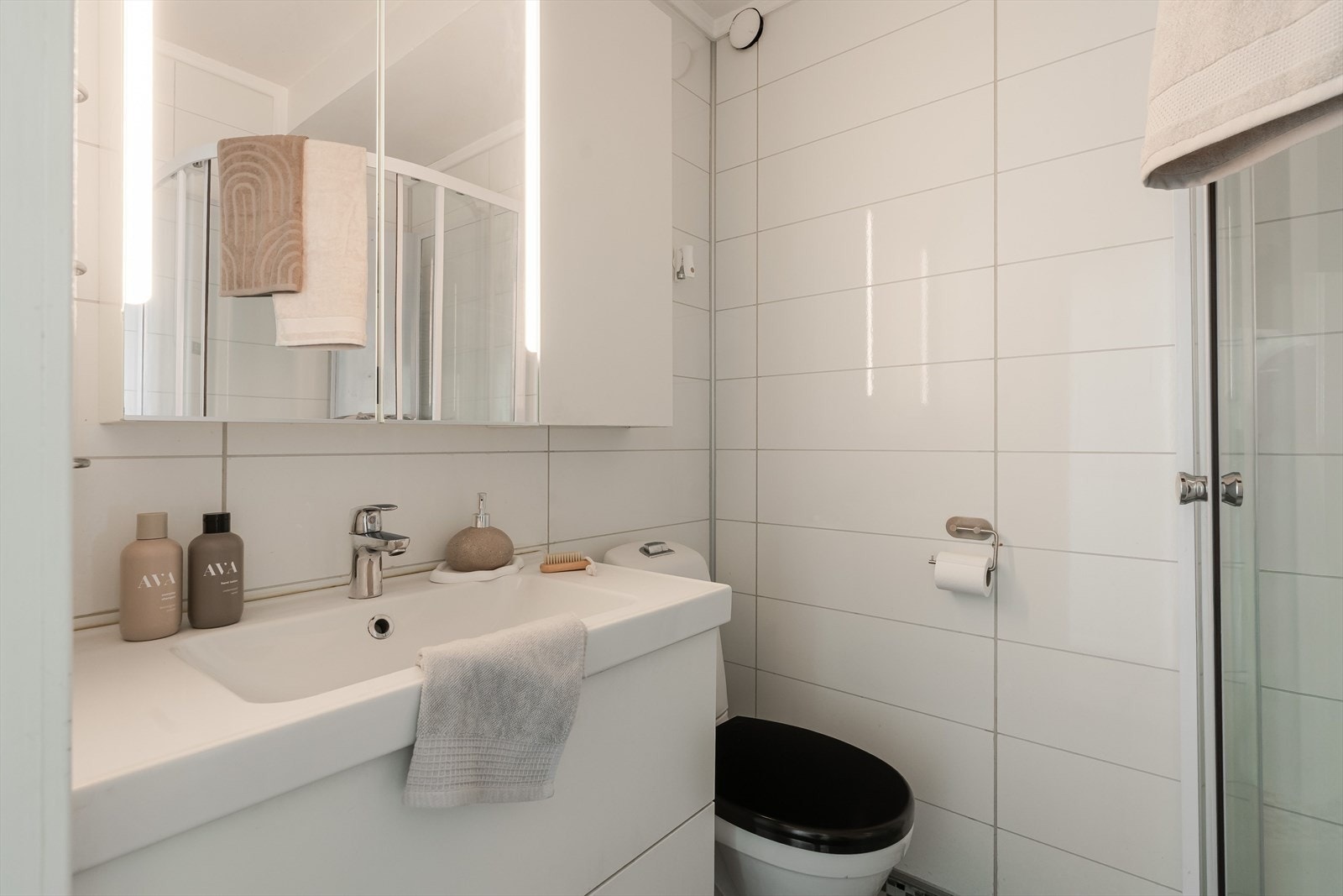 Badet er kompakt og funksjonelt innredet, med flislagte overflater, servantinnredning med speilskap, toalett og dusjkabinett. Galleribilde