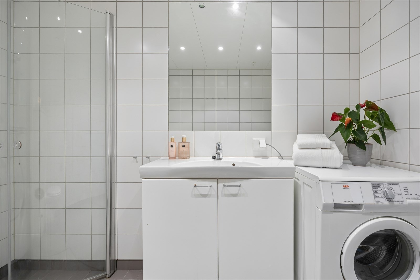 Badet er utstyrt med vegghengt toalett, dusjhjørne med innfellbare glassdører og servant nedfelt i innredning med underskap. Opplegg for vaskemaskin. Galleribilde