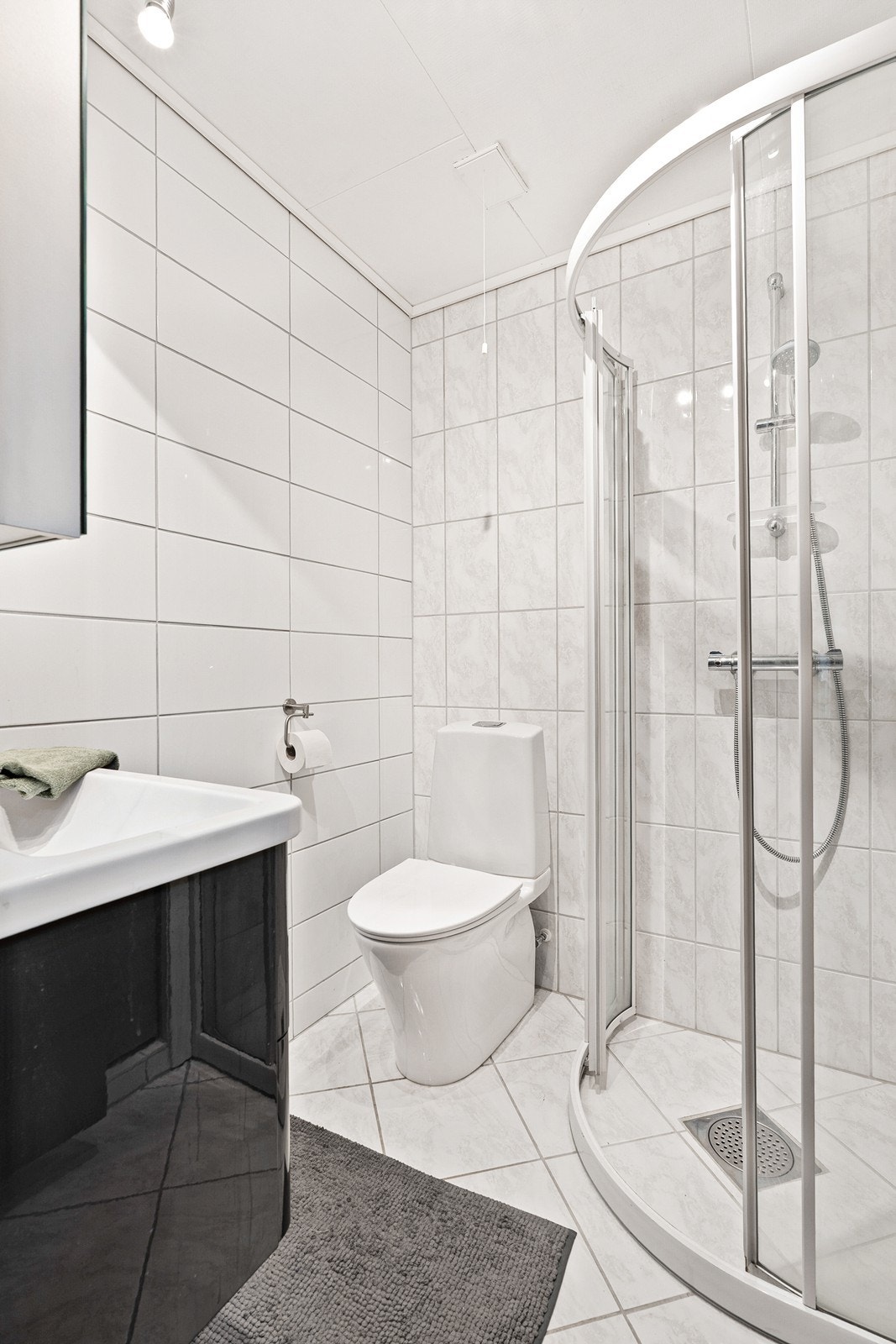 Badet i 1. etasje har keramiske fliser på gulv, servantinnredning, dusjsone og gulvstående toalett. Servant fra 2017 og toalett fra 2023. Galleribilde