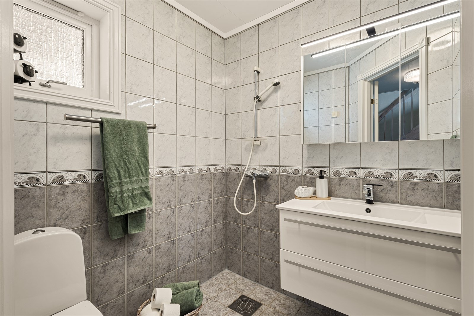 Badet er av god størrelse og er innredet med servant med møblement og speil, belysning, toalett og dusjgarnityr. Galleribilde