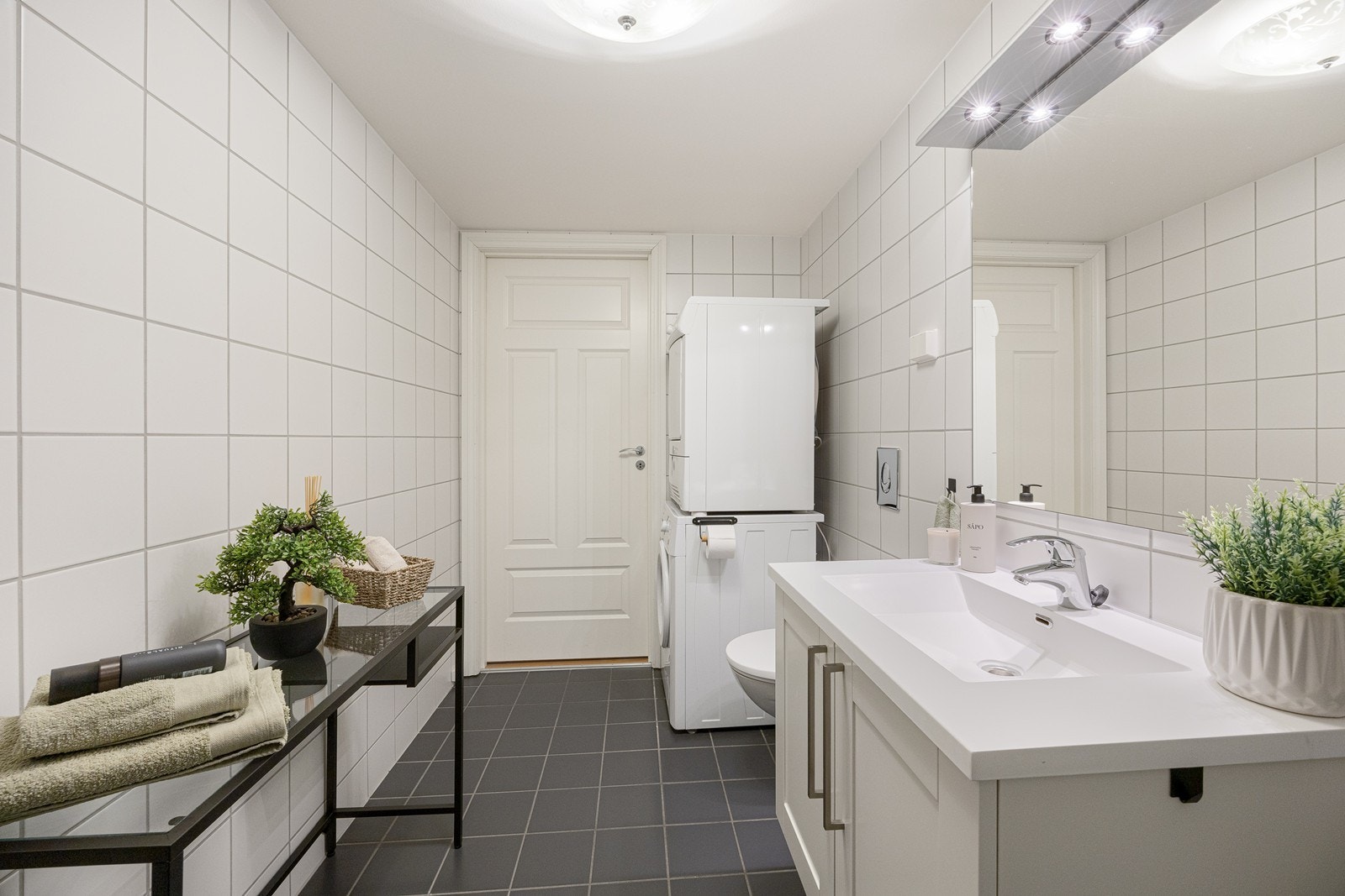 Badet er innredet med hvite veggfliser og mørke gulvfliser for en fin kontrast. Det er opplegg for vaskemaskin og det er varmekabler i gulvet. Galleribilde