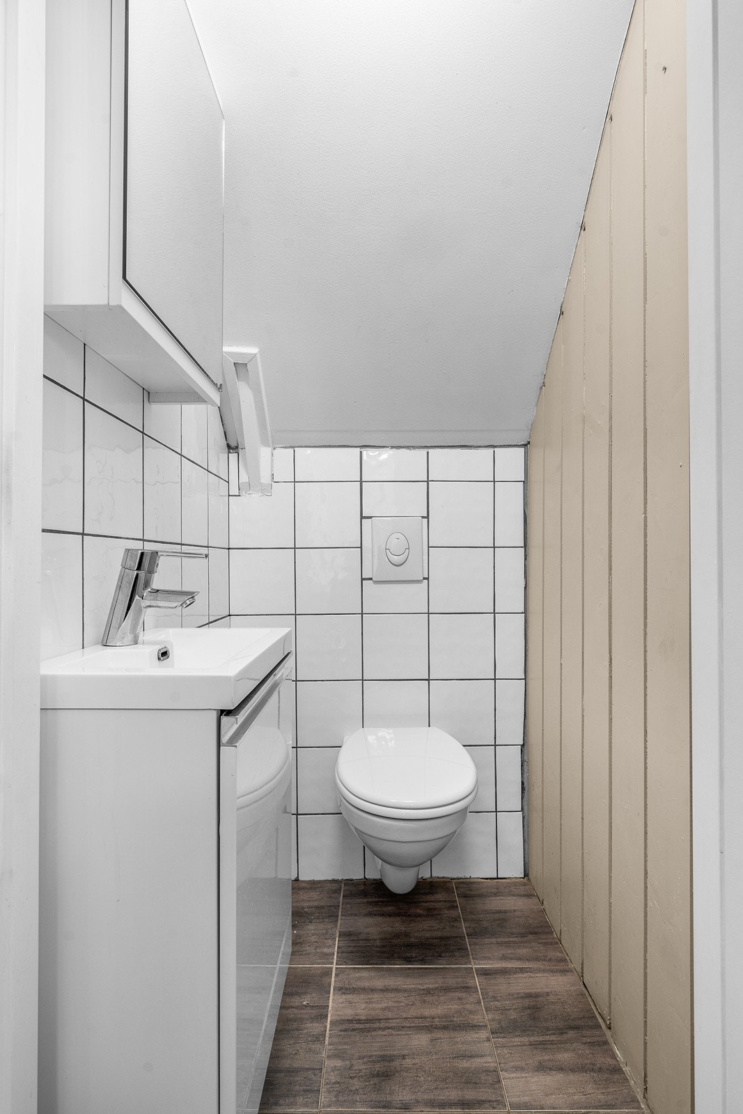 Eget WC-rom under trappen i underetajse. Rommet har fliser på gulv og panel og fliser på vegger. Vegghengt wc og servant på vegg Galleribilde