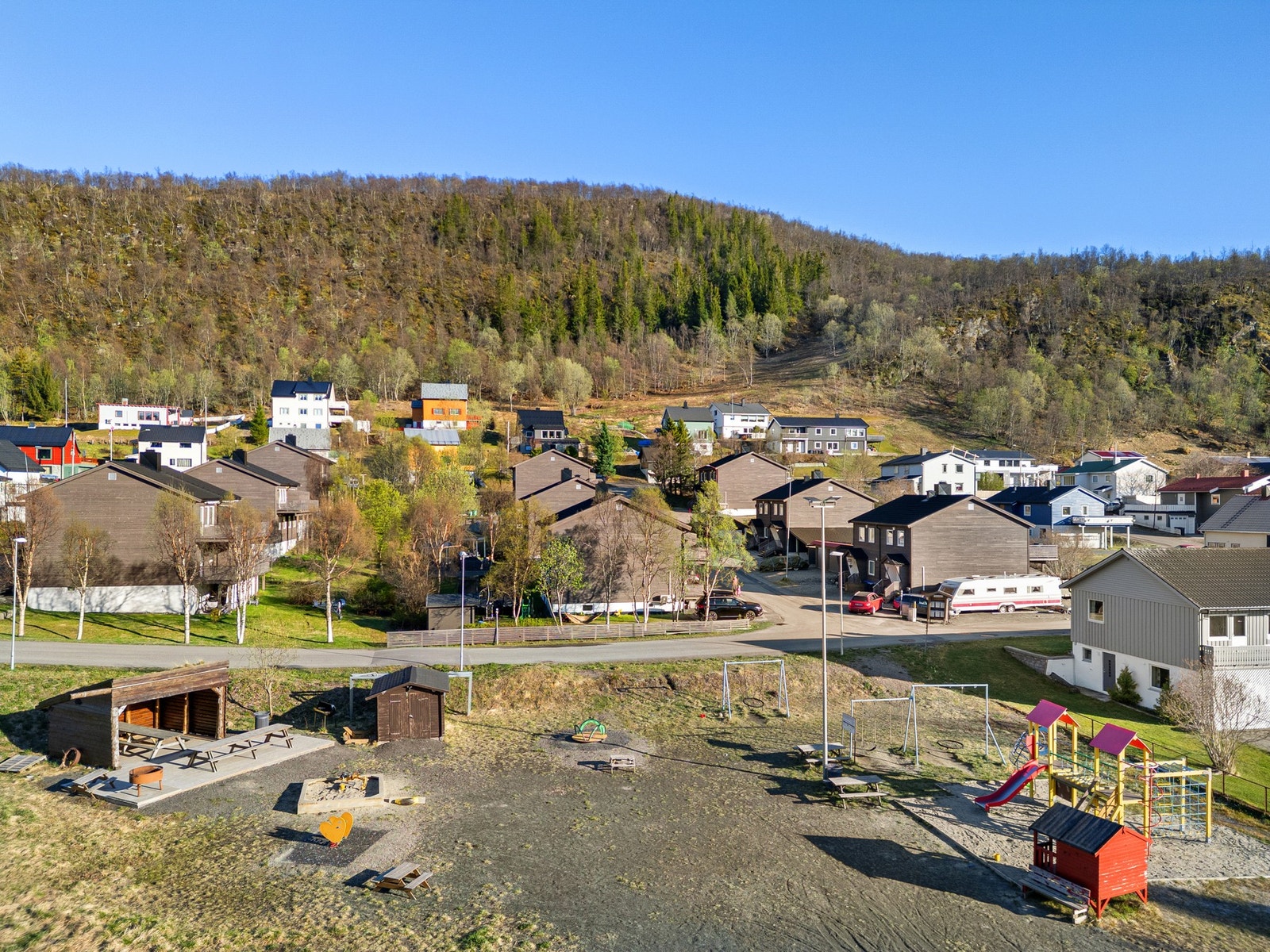 Lekeplass rett ved siden av med flere lekestativer, sandkasse, gapahuk og sittebenker Galleribilde