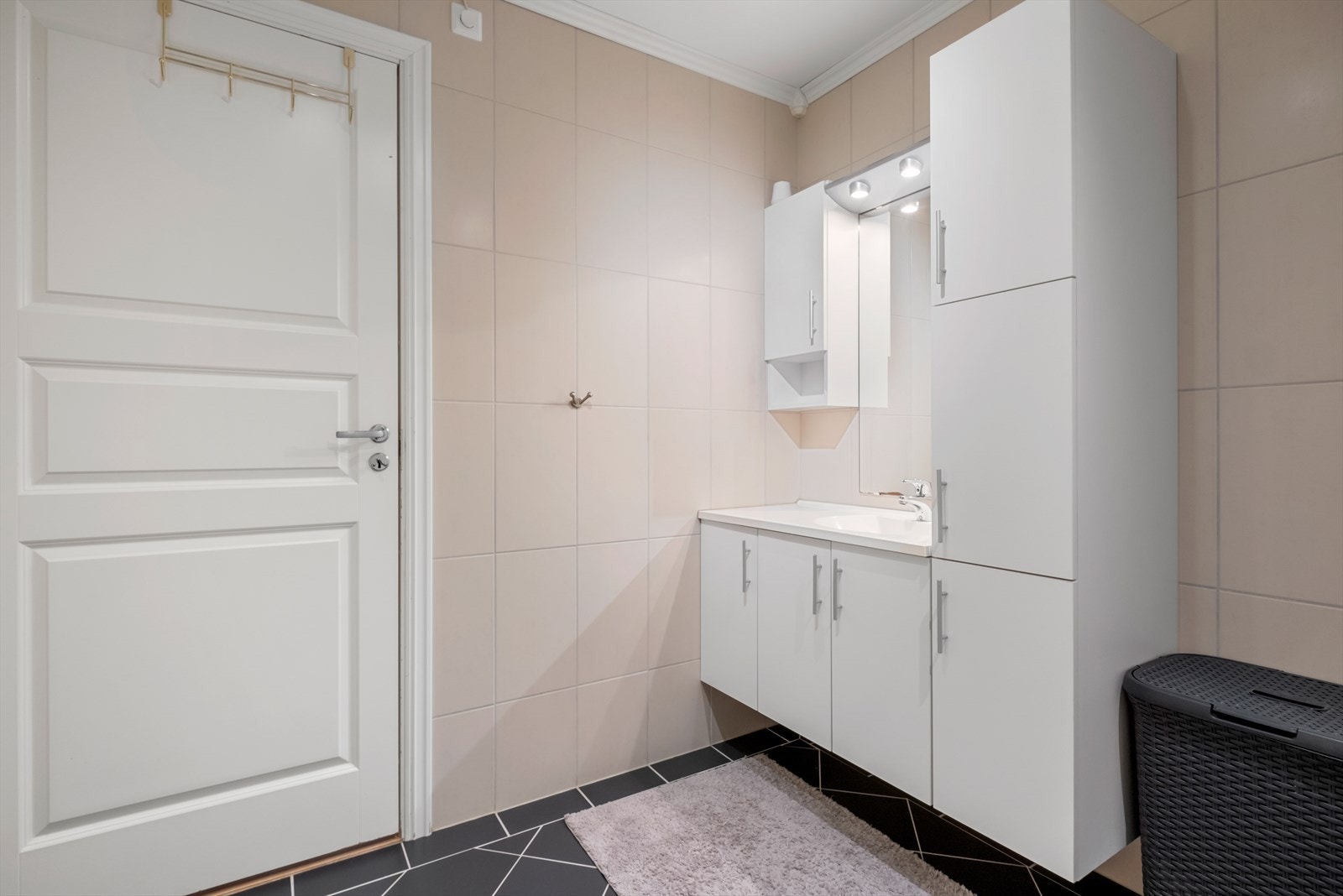 Badet er utstyrt med dusjkabinett fra 2019, veggmontert toalett, speil, servantskap med heldekkende servant og opplegg for tørketrommel og vaskemaskin. Galleribilde
