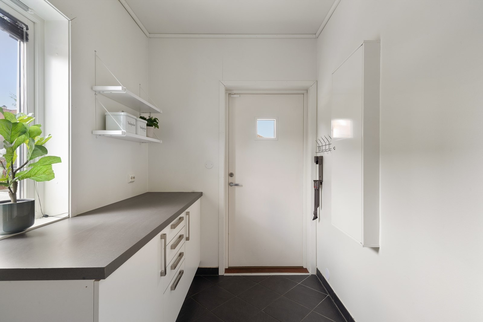 Rommet er flislagt og utstyrt med utslagsvask, samt opplegg for både vaskemaskin og tørketrommel. Med en romslig benkeplate, underskap og overskap, er det enkelt å holde orden på klesvasken. Galleribilde