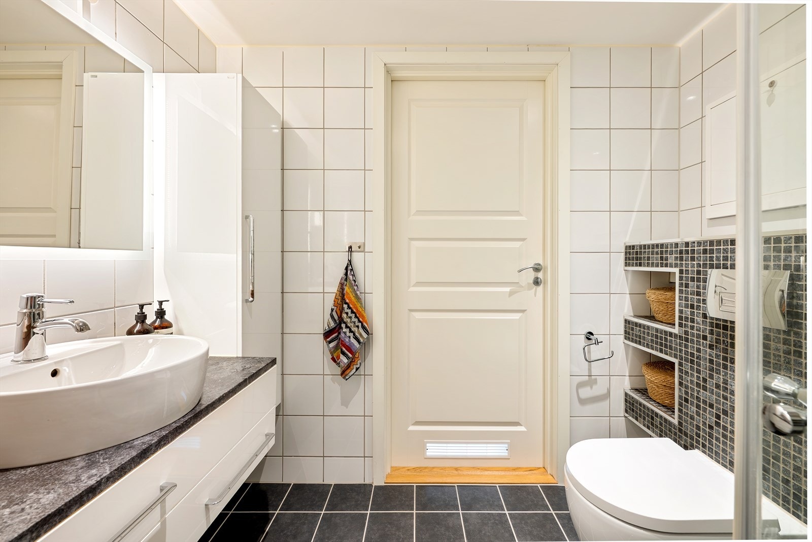 Badet er utstyrt med vegghengt toalett, dusjhjørne med glassdører og opplegg for vaskemaskin. Galleribilde