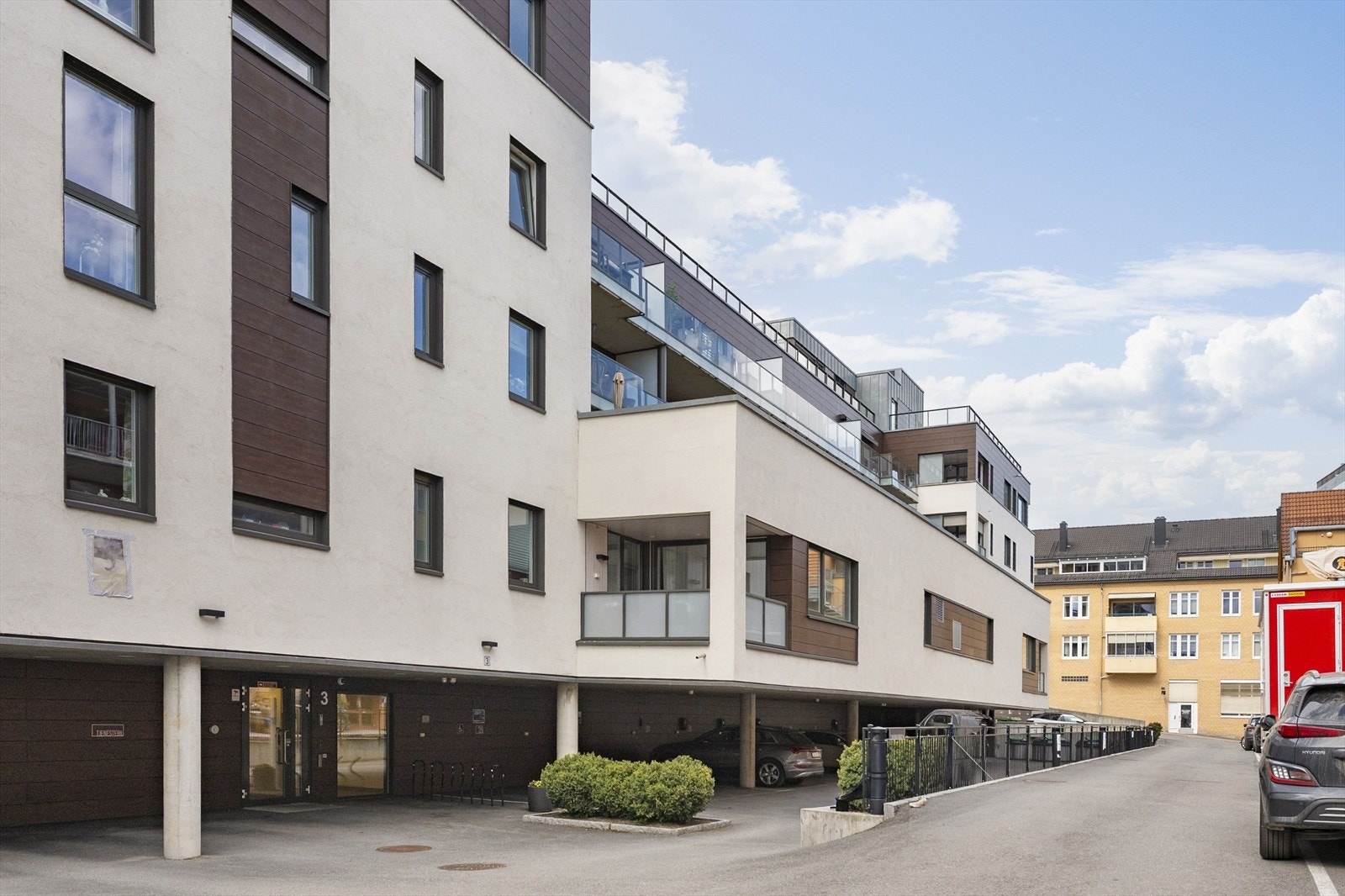 Inngang fra bakkeplan med asfalt, sykkel og bilparkering. Galleribilde