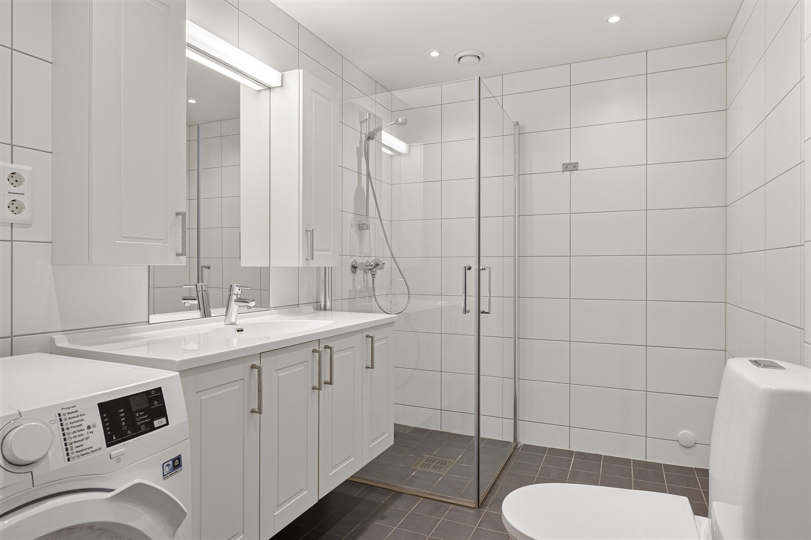 Pent helfliset baderom med downlights i himlingen og opplegg for vaskemaskin. Galleribilde