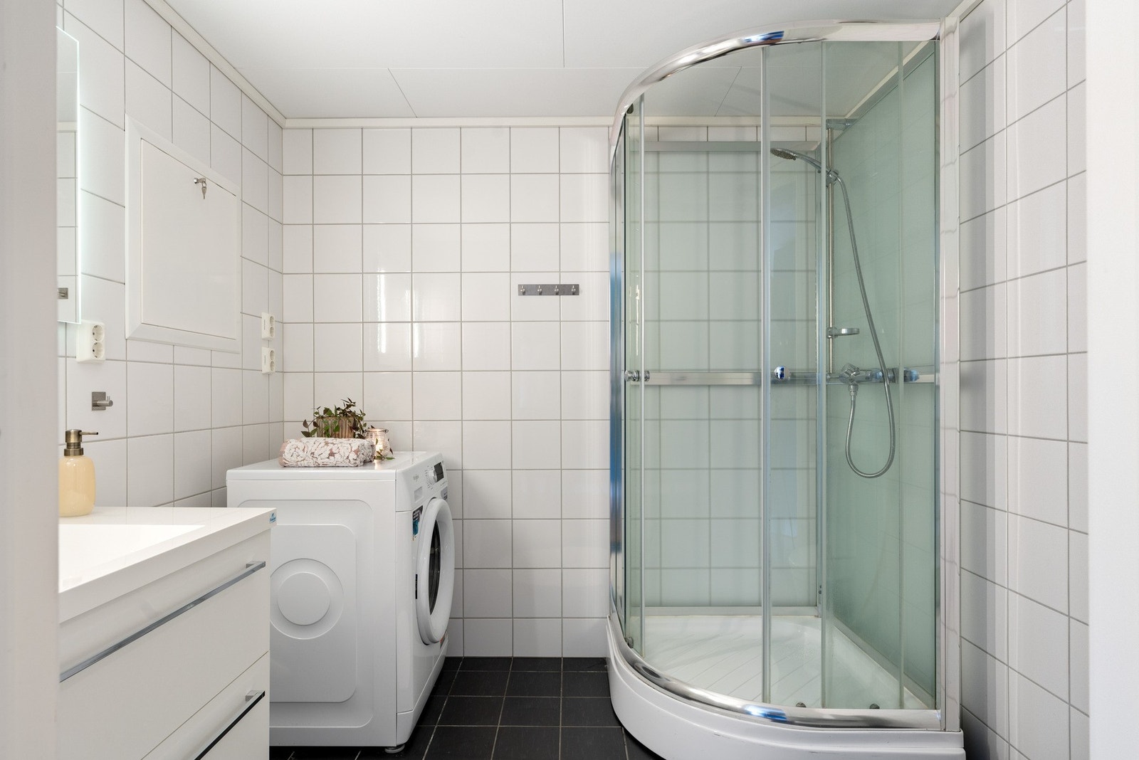 Flislagt baderom med dusjkabinett, moderne innredning og opplegg til vaskemaskin. Galleribilde