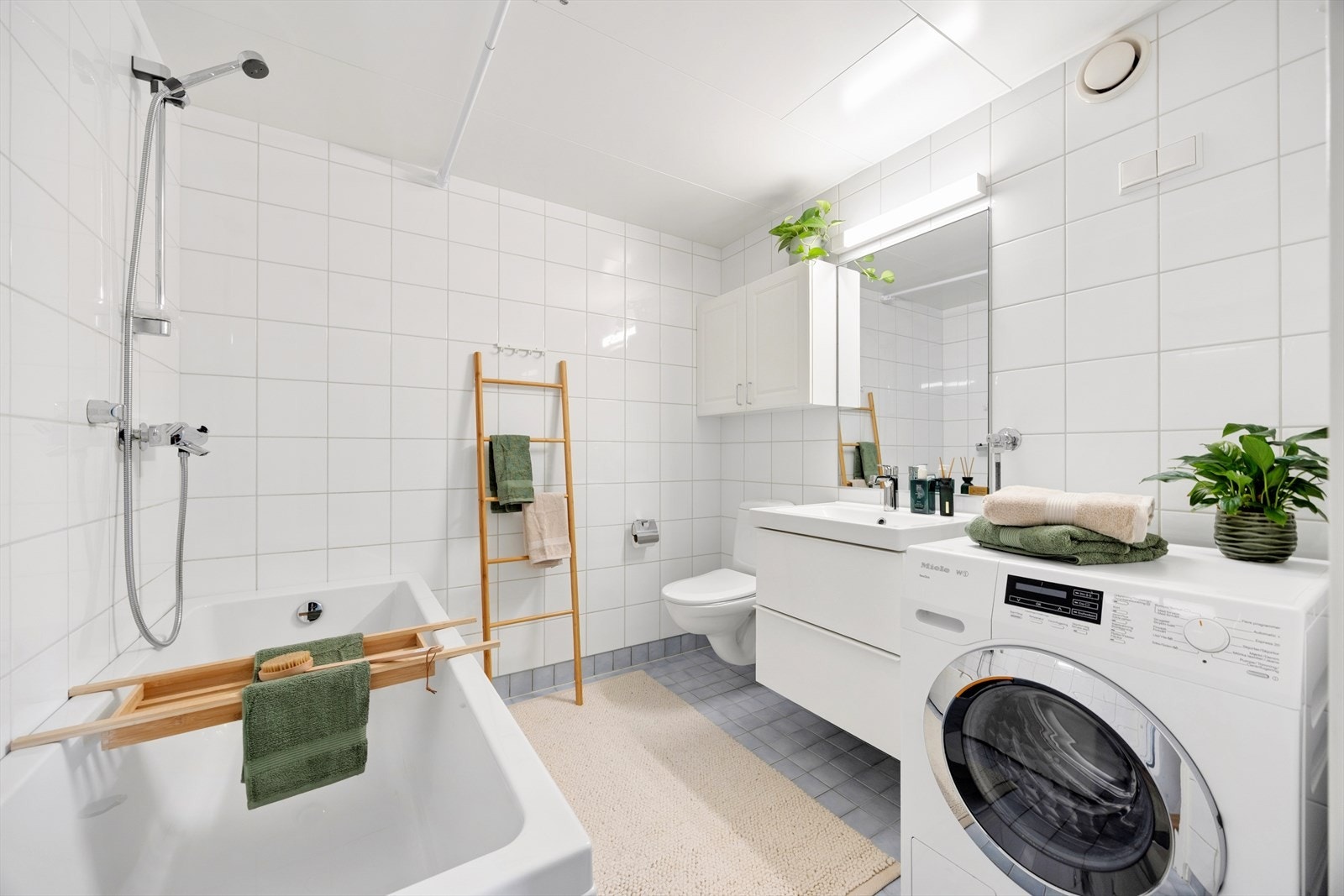 Flott bad med fliser på vegger og gulv, som gir et moderne og stilrent uttrykk. Det er montert vegghengt toalett og dusjhjørne med badekar. Det er opplegg og god plass for vaskemaskin og tørketrommel. Galleribilde