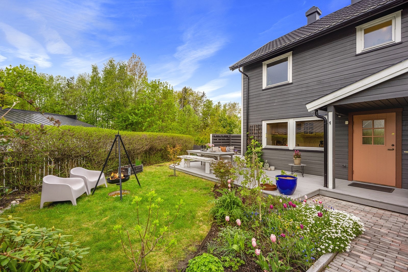 Tomten er pent opparbeidet med plen, beplantning og en stor terrasseplatting. Galleribilde