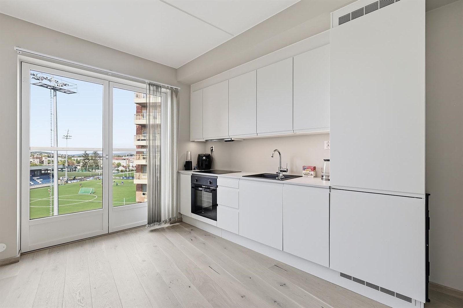 Pent kjøkken med hvite fronter. Det medfølger oppvaskmaskin, komfyr, koketopp og kjøleskap/fryser. Galleribilde