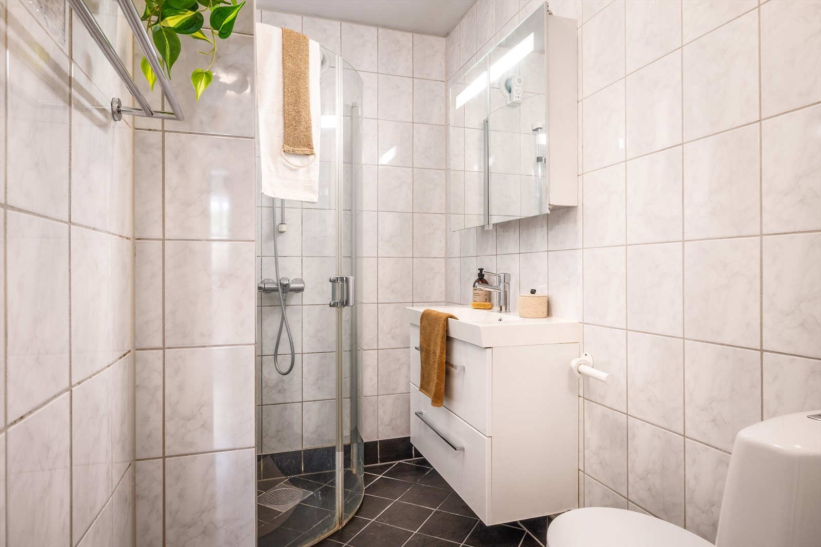 Badet er flislagt og innredet med servant, toalett og dusjhjørne. Galleribilde