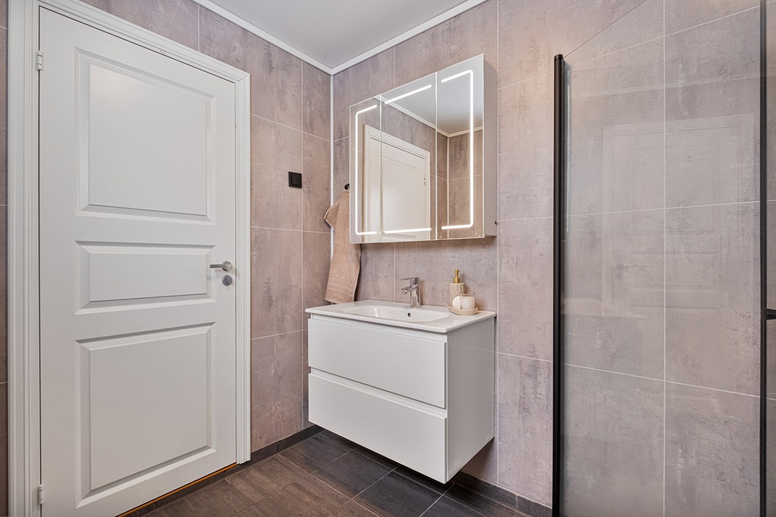 Badet er utstyrt med heldekkende servant, speilskap med lys, veggmontert toalett og dusjvegger av glass. Det er mekanisk avtrekk. Galleribilde