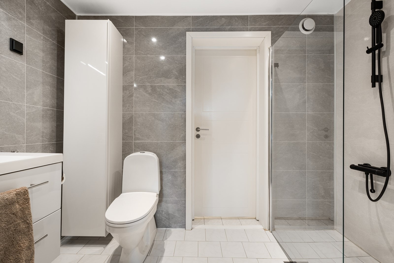 Badet har fliser på gulv og baderomsplater på vegger og er utstyrt med toalett, dusjhjørne og baderomsmøbler. Galleribilde