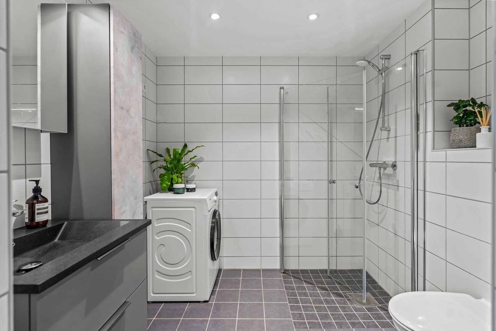 Badet er delikat innredet med grå gulvfliser, hvite veggfliser, gulvvarme og downlights. Galleribilde