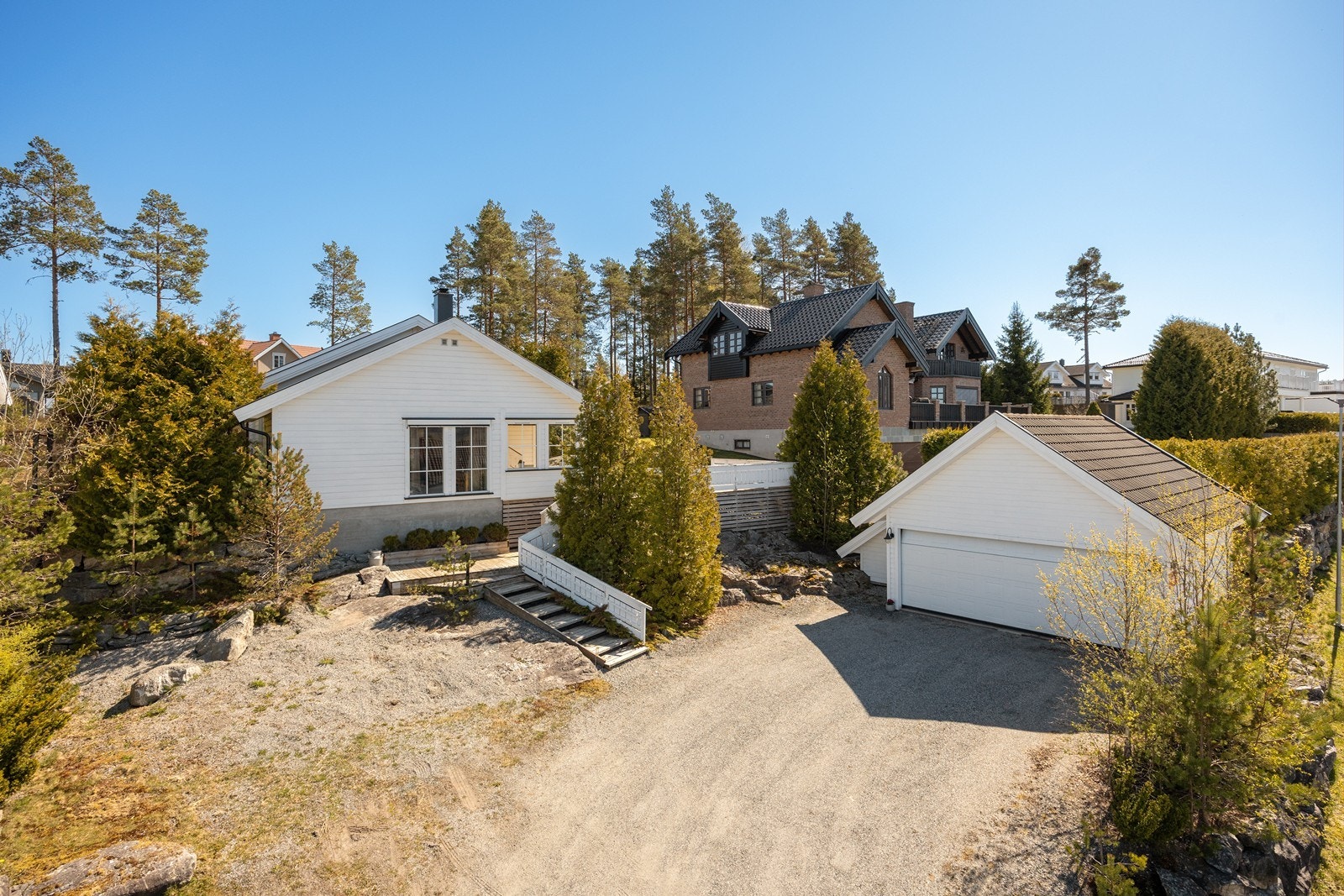 Eneboligen ligger på en romslig tomt, der gressplenen og diverse beplantning suppleres av fjell i dagen og naturlig vegetasjon. Foran garasjen har eiendommen en gruslagt gårdsplass. Galleribilde