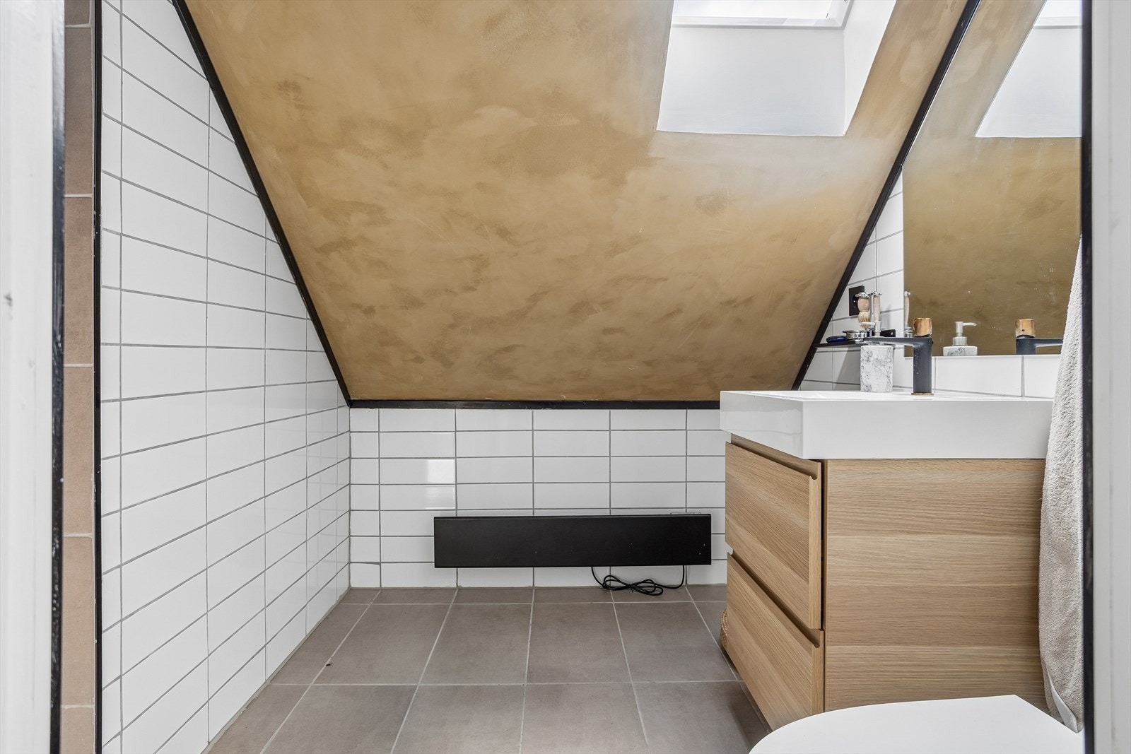 Baderomsinnredning med servant og underskap. Lyset kommer fra spotter og et Velux takvindu. Galleribilde