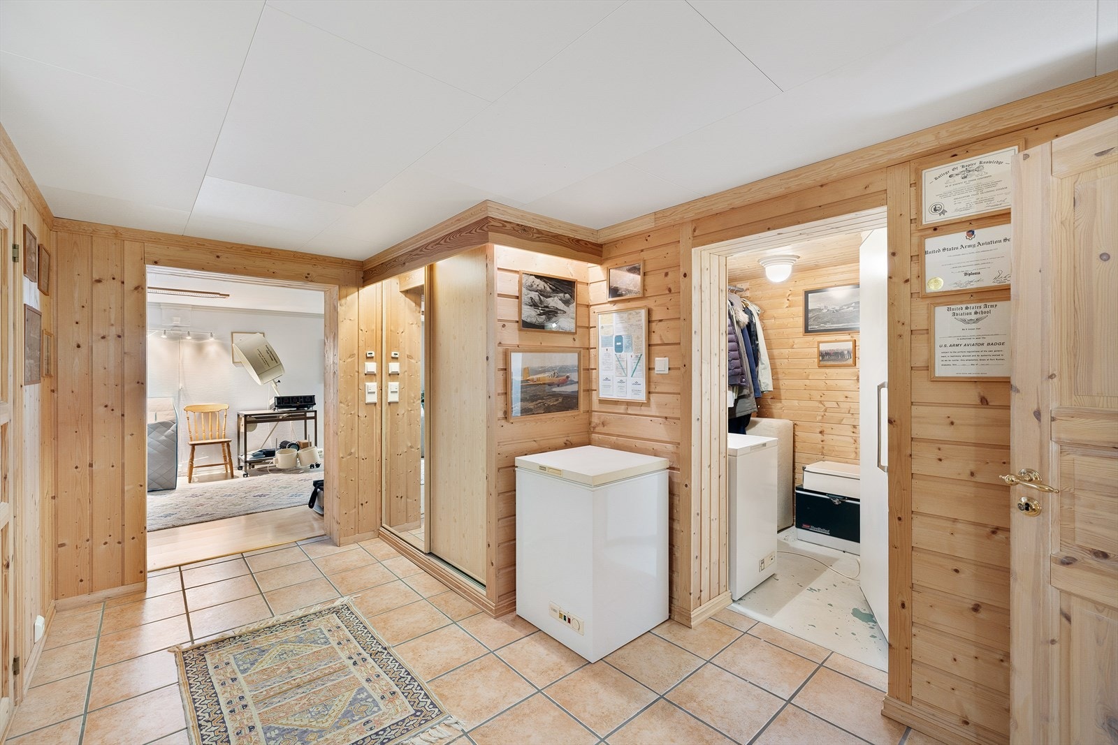 Romslig gang i kjelleretasjen med flislagt gulv, panelvegger og integrert skyvedørsgarderobe. Galleribilde