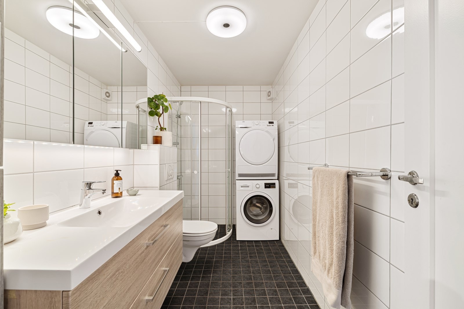 Badet inneholder baderomsmøbel med laminerte fronter, heldekkende servant og ett-greps blandebatteri, speilskap med belysning, veggskap, vegghengt toalett, opplegg for vaskemaskin/tørketrommel og buet dusjhjørne med dusjgarnityr. Galleribilde
