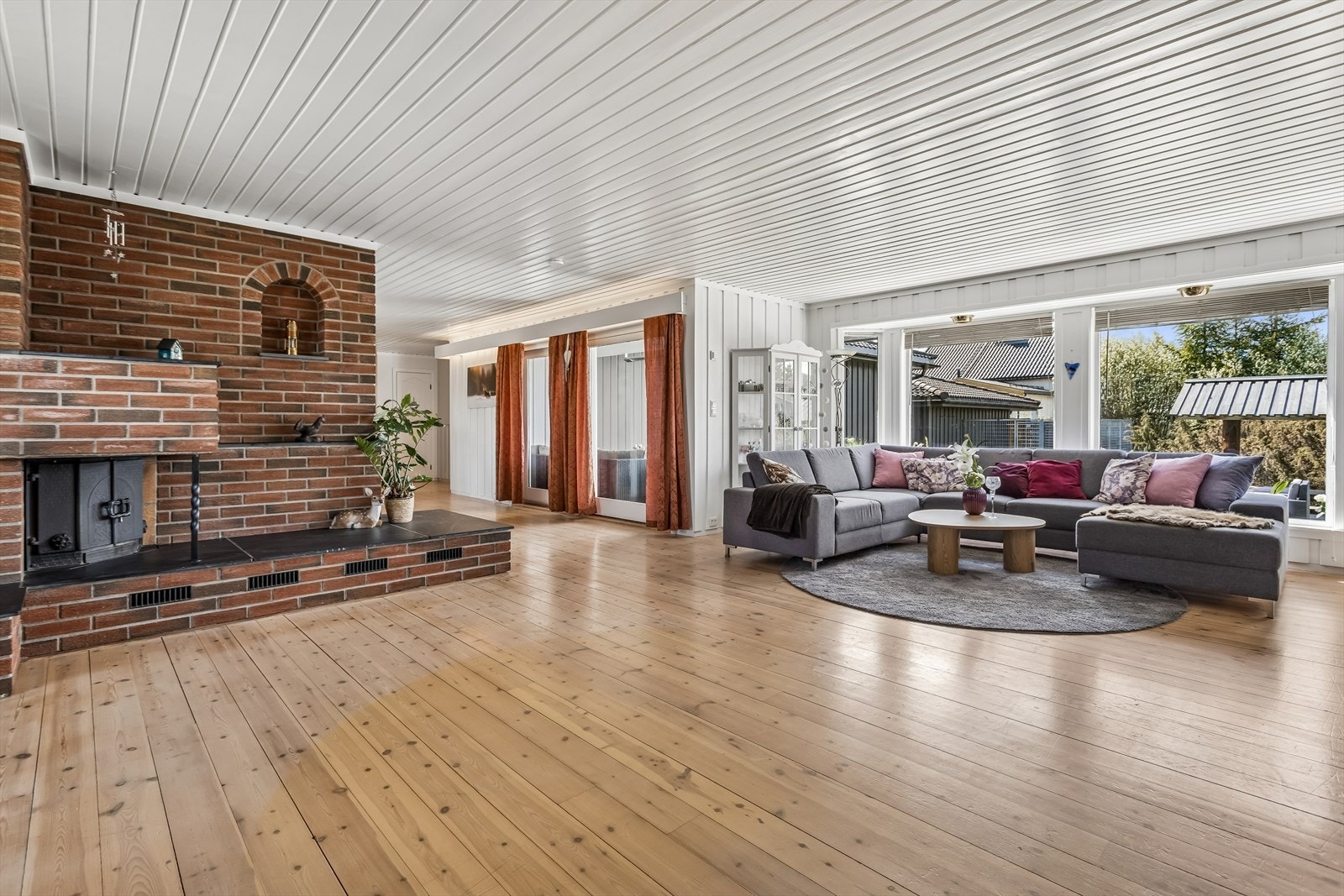 Romslig stue med store vinduer og plass for flere sittegrupper. Galleribilde