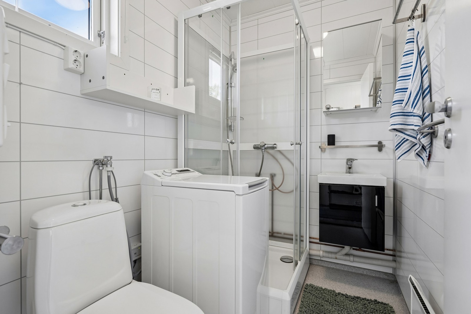 Badet har vinylbelegg på gulv og vegger med våtromspanel, samt folierte plater i himlingen. Rommet er utstyrt med dusjkabinett, gulvmontert toalett, servant med innredning og opplegg for vaskemaskin. Galleribilde