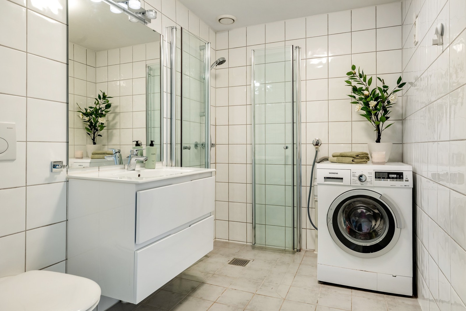 Leiligheten har et pent bad med flislagte vegger og flislagt gulv, utstyrt med elektriske varmekabler. Badet er innredet med nedfelt servant på skuffeseksjon, speil med lys, vegghengt toalett og dusjvegger/hjørne. I tillegg har badet opplegg for vaskemas Galleribilde