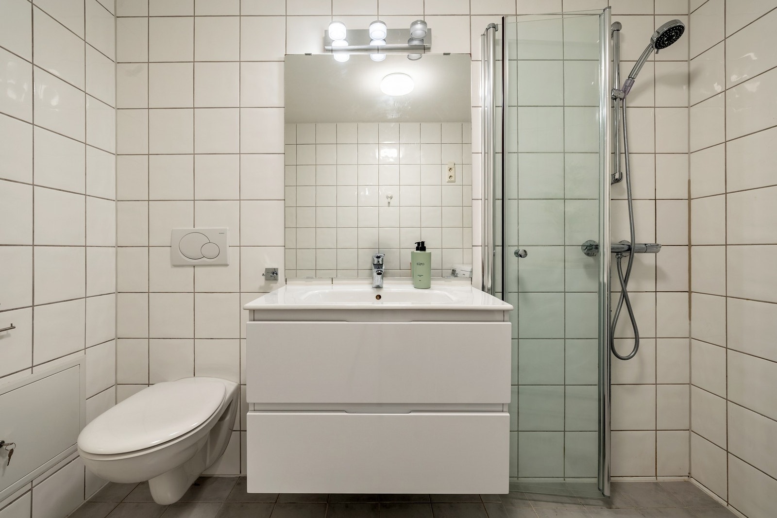 Leiligheten har et pent bad med flislagte vegger og flislagt gulv, utstyrt med elektriske varmekabler. Badet er innredet med nedfelt servant på skuffeseksjon, speil med lys, vegghengt toalett og dusjvegger/hjørne. I tillegg har badet opplegg for vaskemas Galleribilde