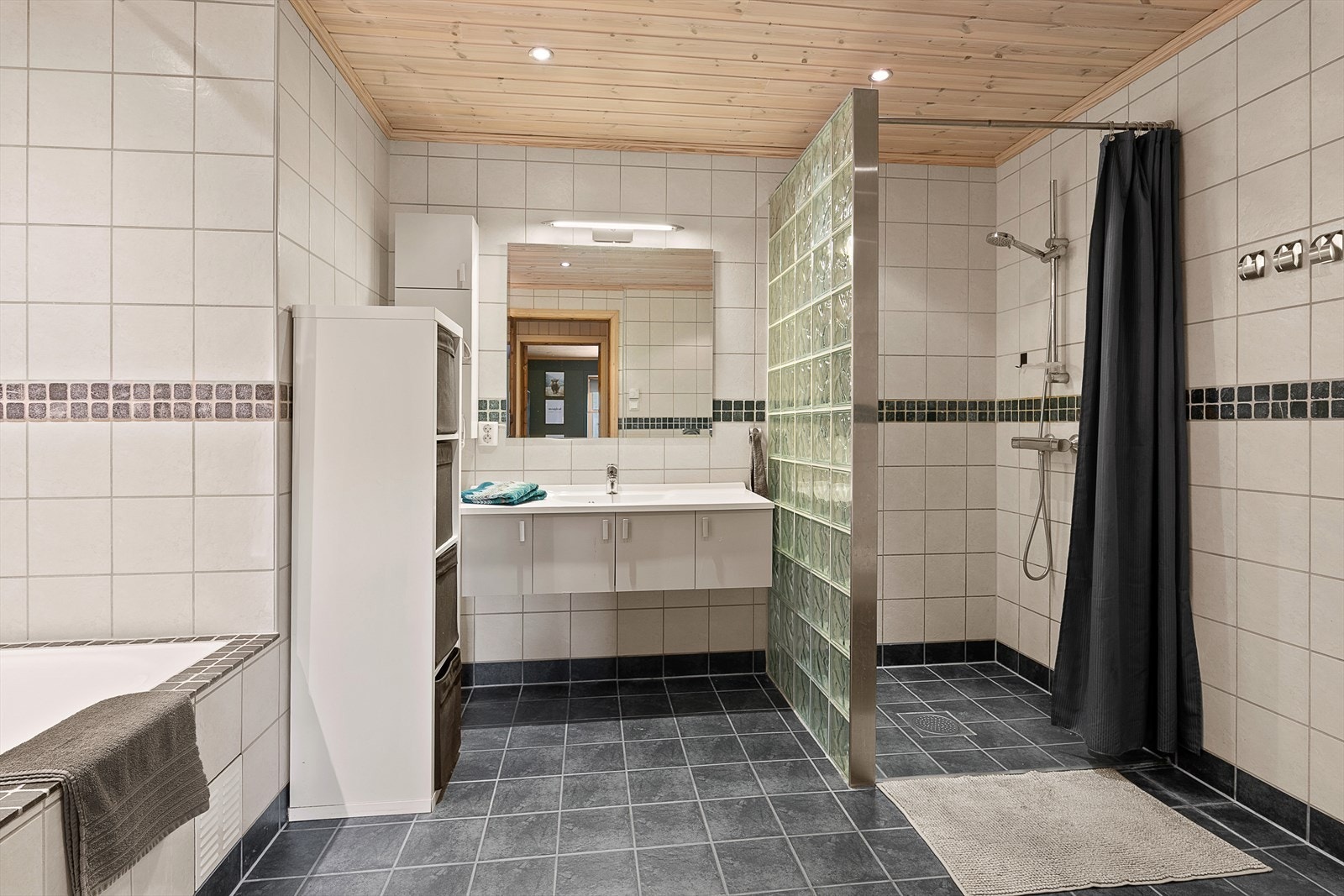 Badet er utstyrt med innebygd badekar, dusjhjørne, servant med tilpassede skap og vegghengt wc. Galleribilde