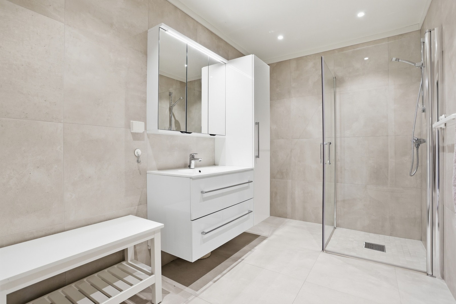 Badet i u.etg. gir det samme flotte inntrykket og er utstyrt med veggmontert toalett, glassdører mot dusjnisje samt dusjgarnityr, innredning med skuffer og heldekkende servant samt vegghengt skap med speil. Galleribilde