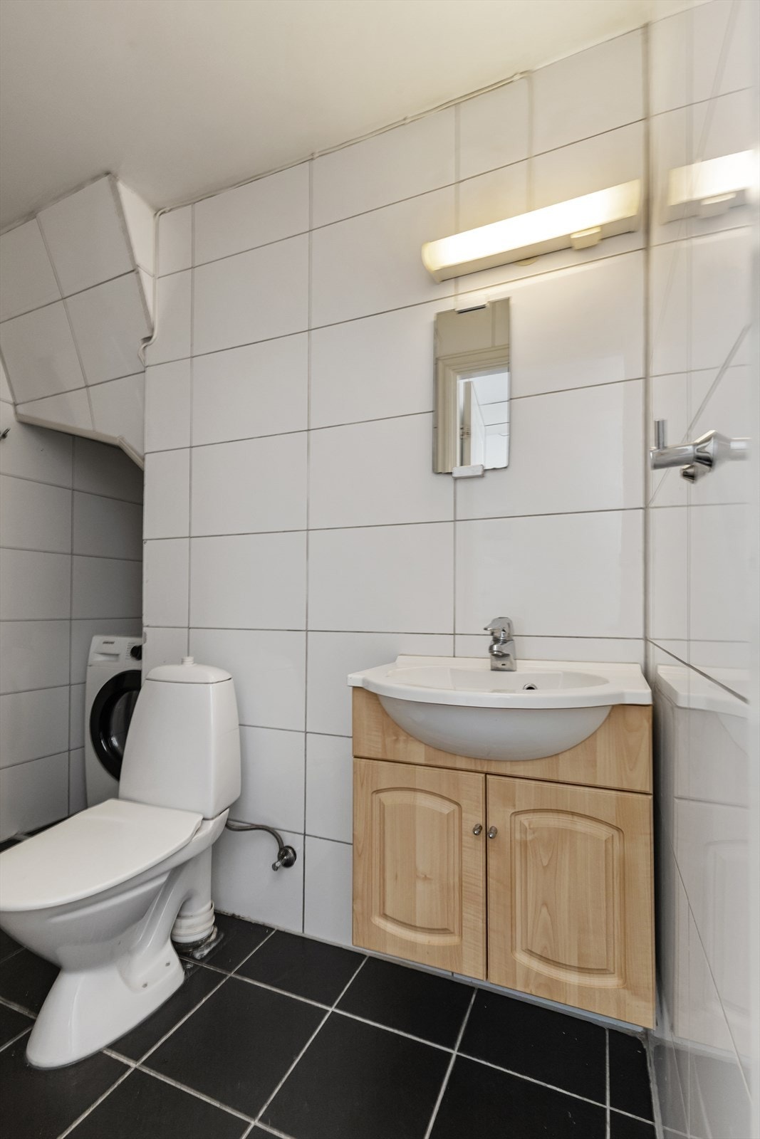 Badet har fliser på gulv og vegger, og er utstyrt med dusjhjørne og opplegg for vaskemaskin. Galleribilde