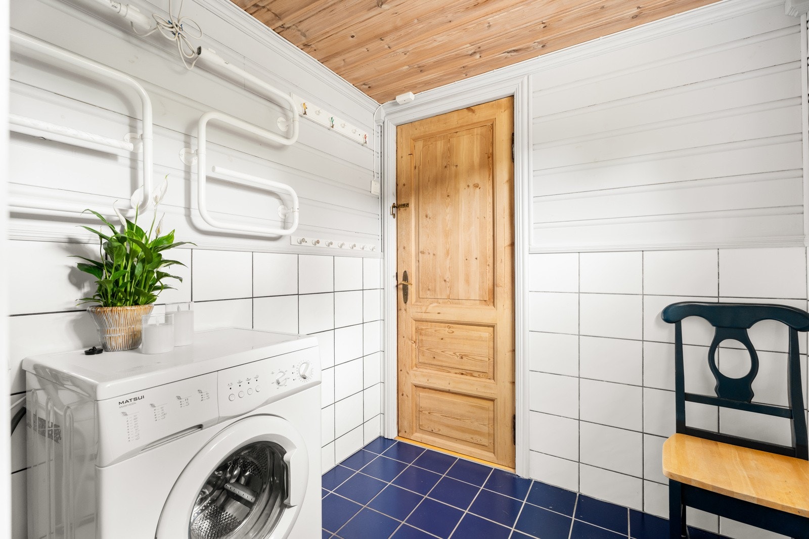 Badet har blå fliser på gulv med gulvvarme, hvite fliser og malt panel på veggene, samt trehvit panel i taket. Galleribilde