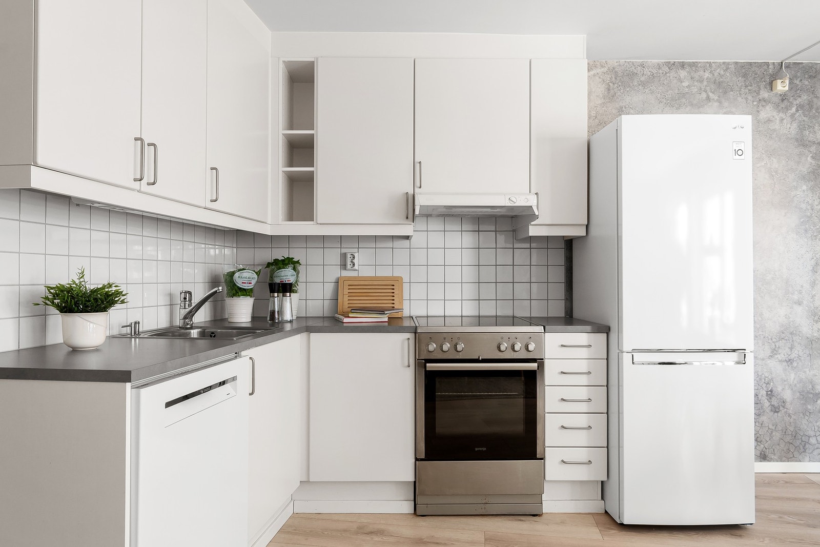 Innredningen består av hvite, glatte
fronter, laminat benkeplate med nedfelt kum i rustfritt stål, belysning under overskap og fliser på
vegg over benkeskap. Frittstående komfyr, kjøl/fryseskap og halvintegrert oppvaskmaskin under
benkeplate. Galleribilde