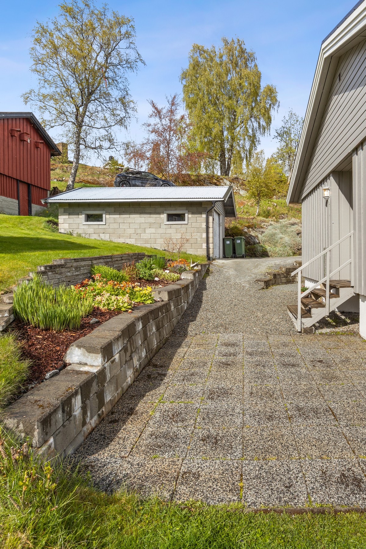 Inngangspartiet er pent opparbeidet med steinbelagt og gruslagt dekke, samt blomsterbed ved mur. Galleribilde