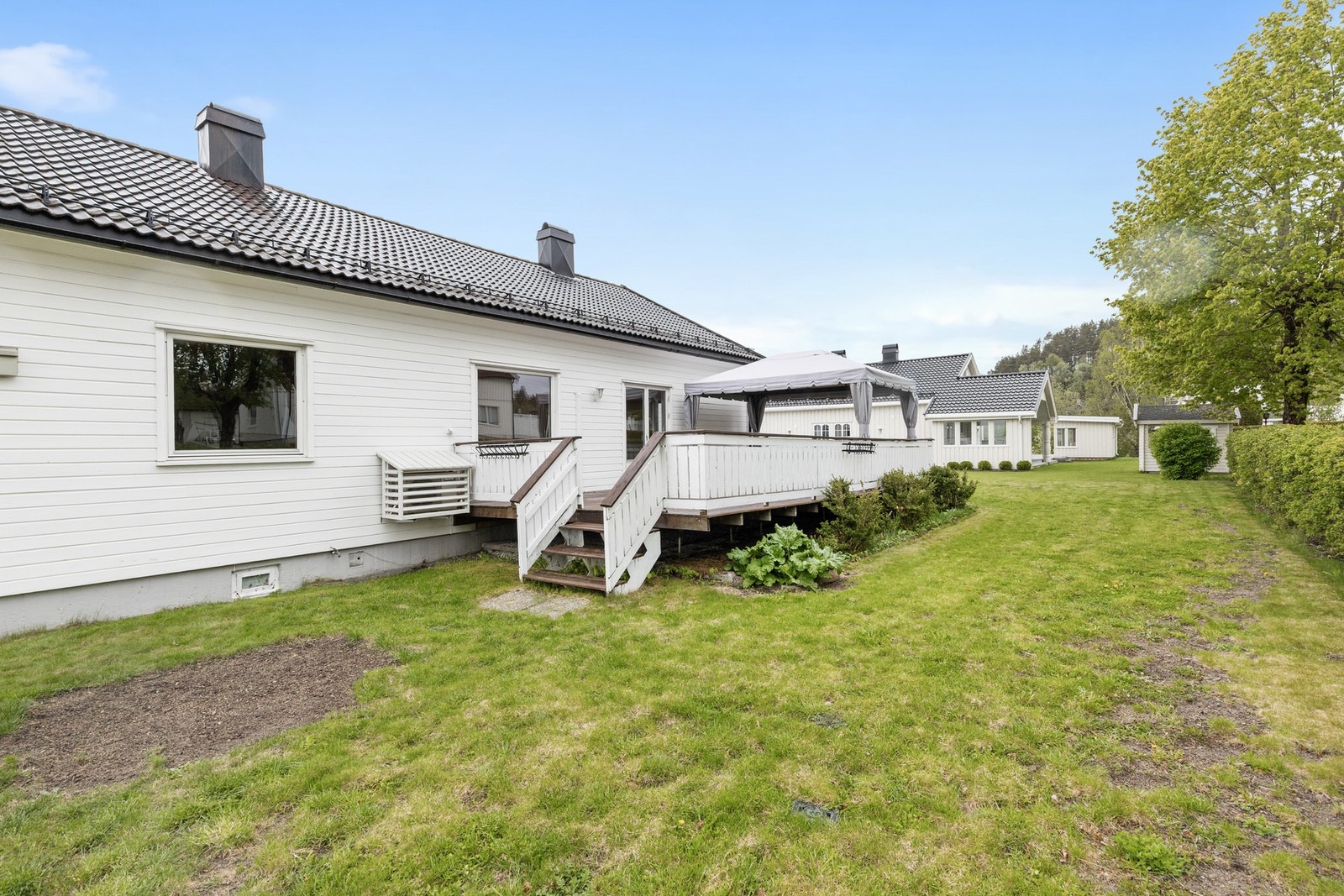 Boligen har fine uteplasser, bl.a. en vestvendt terrasse og stor gressplen skjermet av hekk Galleribilde