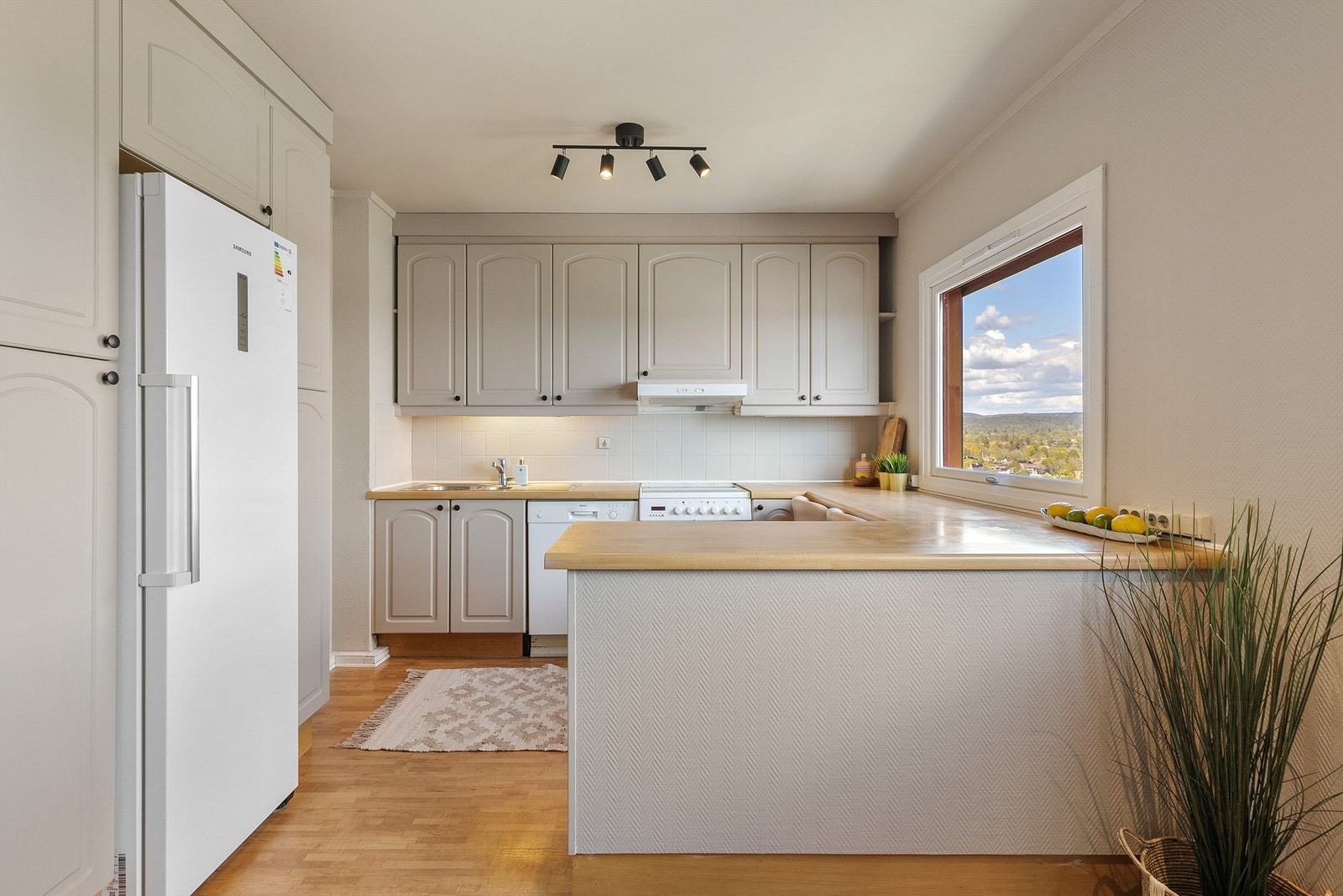 Kjøkkeninnredning med profilerte fronter. Benkeplate med laminert overflate. Kjøkkenvask med armatur. Frittstående komfyr, oppvaskmaskin og kjøleskap. Ventilator i overskap. Galleribilde