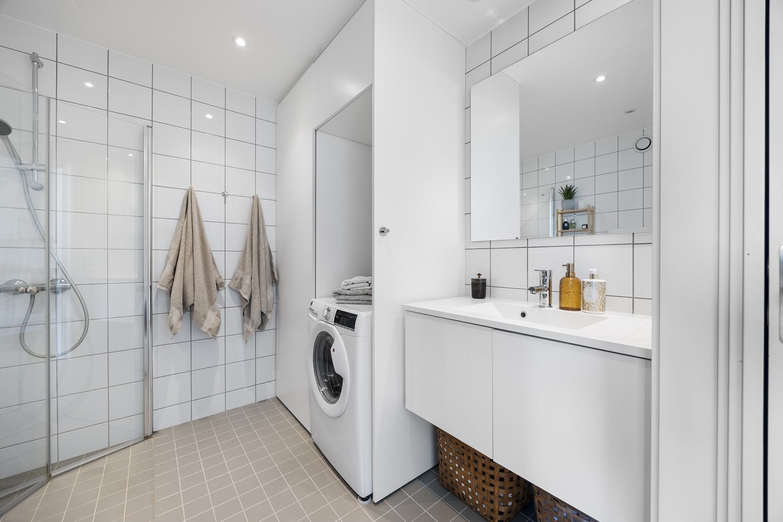 Lekkert, flislagt bad med downlights og varmekabler i gulv. Praktisk nisje til vaskemaskin og tørketrommel. Badet er innredet med vegghengt wc, dusjnisje med innfellbare dusjdører og hvit baderomsinnredning og speil Galleribilde