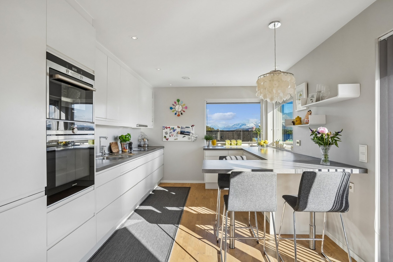 Flott kjøkkeninnredning fra Norema med hvite glatte fronter og fuktbestandige plater på vegg over laminat benkeplate. Galleribilde