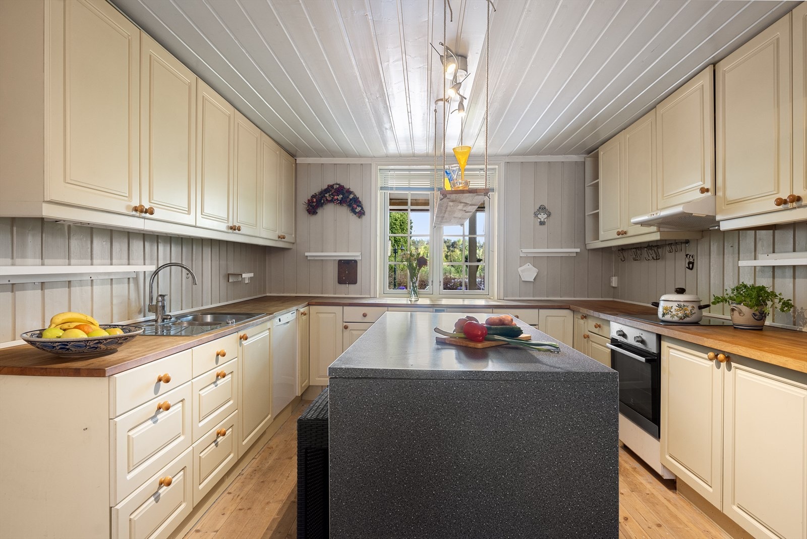 Kjøkkeninnredningen har profilerte fronter i offwhite, heltre benkeplater og nedfelt oppvaskkum i rustfritt stål med ettgreps kjøkkenarmatur i krom. Kjøkkenøy fra Norema med laminatbenkeplate i granitt-look gir ekstra arbeidsflate og oppbevaringsplass. Galleribilde