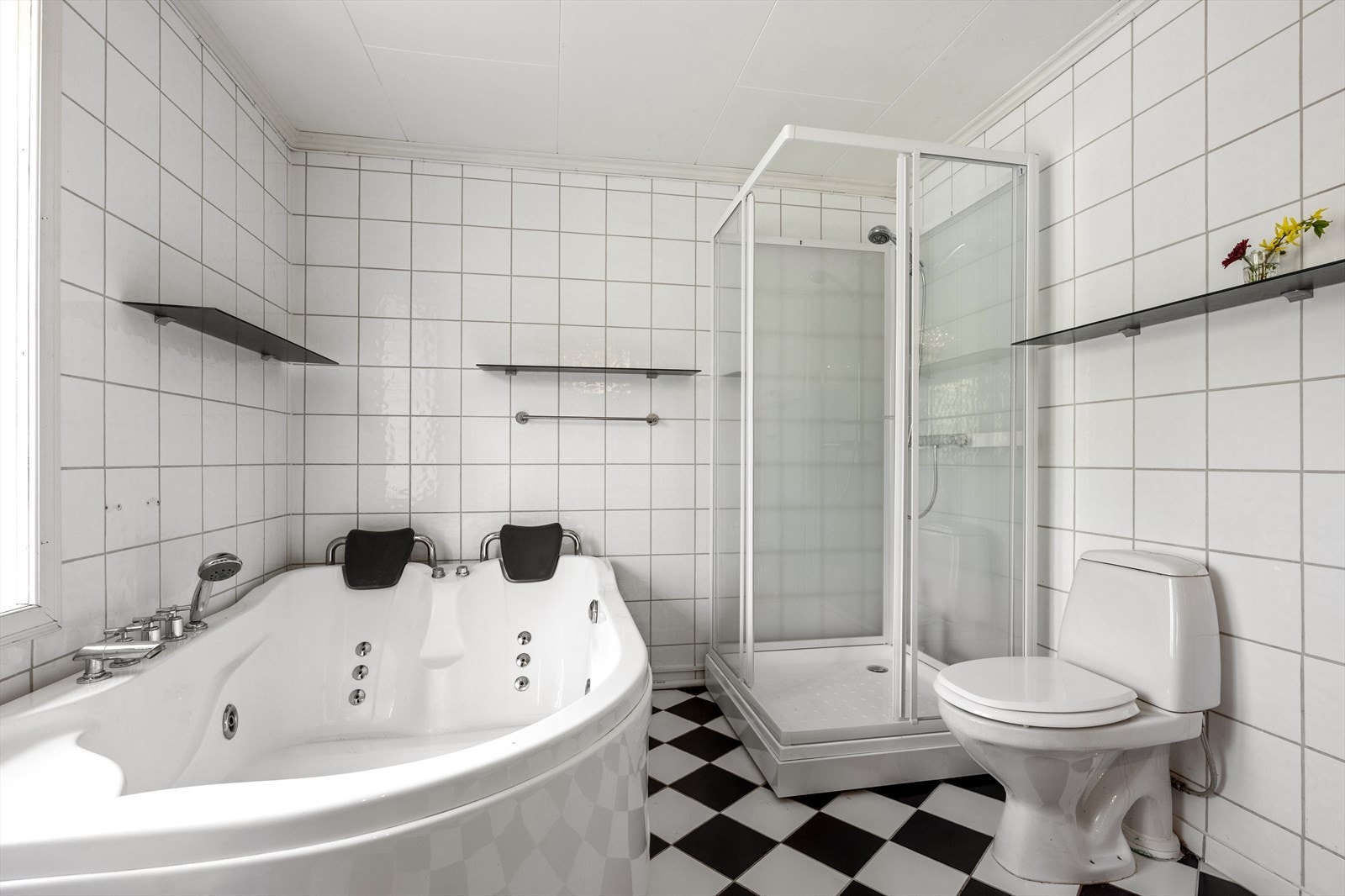 Badet er utstyrt med dusjkabinett, badekar med massasjefunksjon, servantskap med mørke fronter og dobbel servant i glass med to ettgreps servantarmaturer. Galleribilde