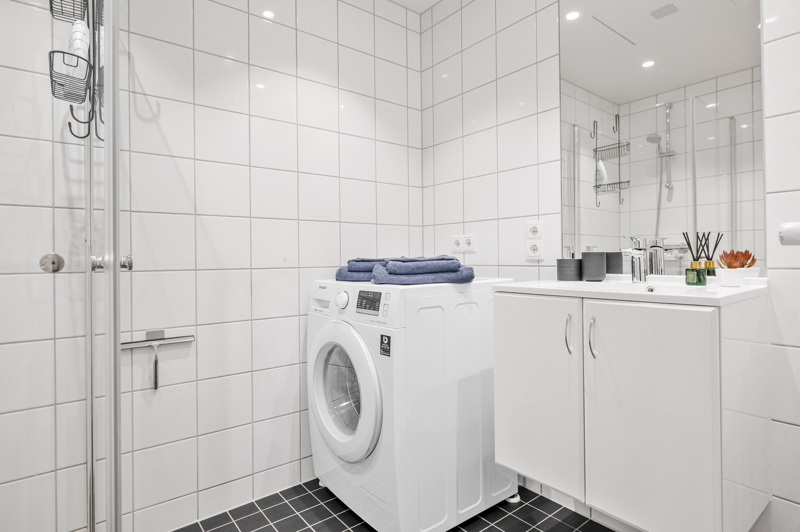 Det er vegghengt servantinnredning med speil med overlys. Baderommet inneholder dusjhjørne med dører, vegghengt toalett og opplegg for vaskemaskin. Galleribilde
