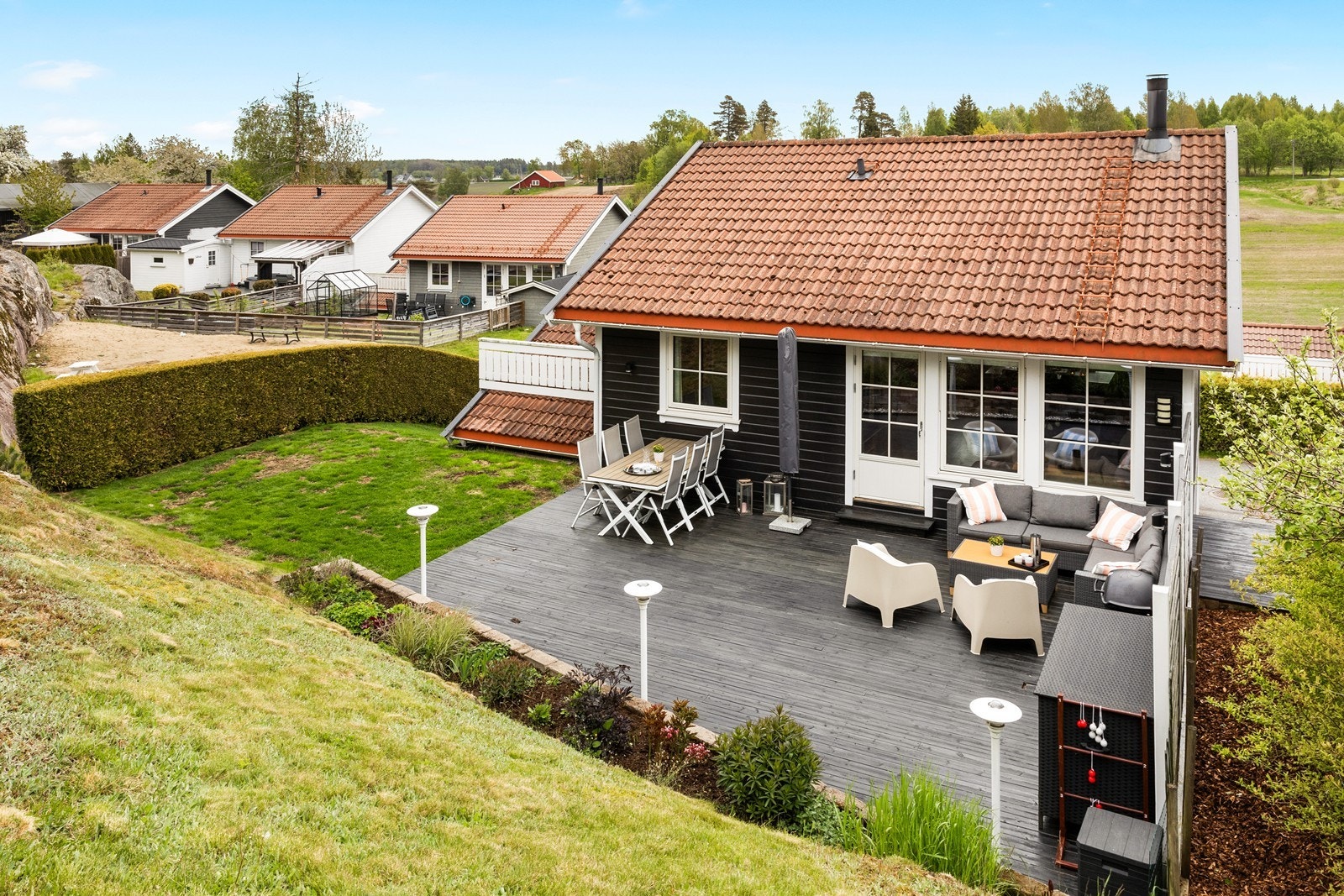 På terrassen er det levegg, utelamper og blomsterbed som følger terrenget, samt et lite trinn ned til grønn hageflekk. Galleribilde