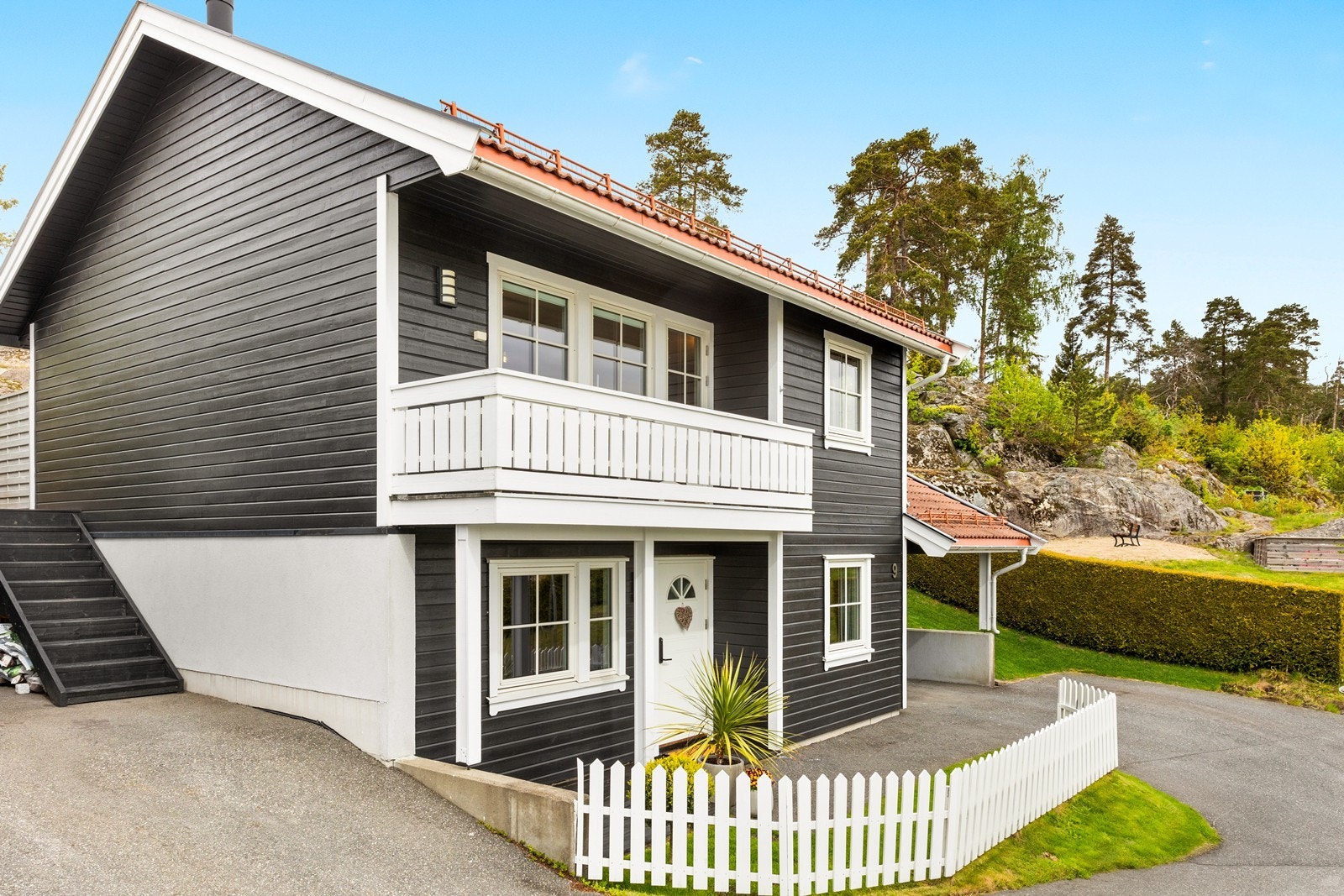 Inngangspartiet er innbydende med hvitt stakittgjerde og overbygd ytterdør kun noen få meter fra carport. Huset ble malt i 2024. Galleribilde
